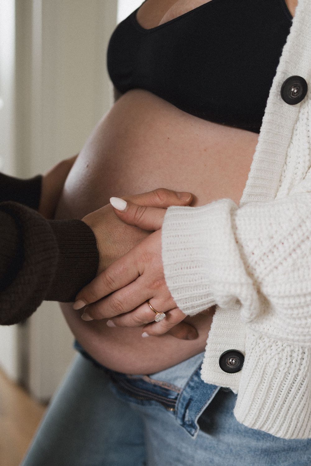 A close-up of a couple's hands tenderly holding a pregnant woman's bare belly, ring visible.