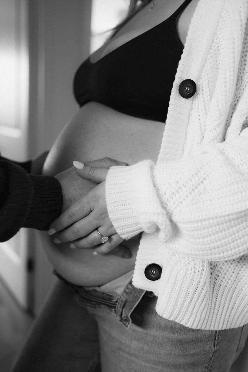 Black and white close-up of a couple's hands gently cradling a pregnant woman's bare baby bump.