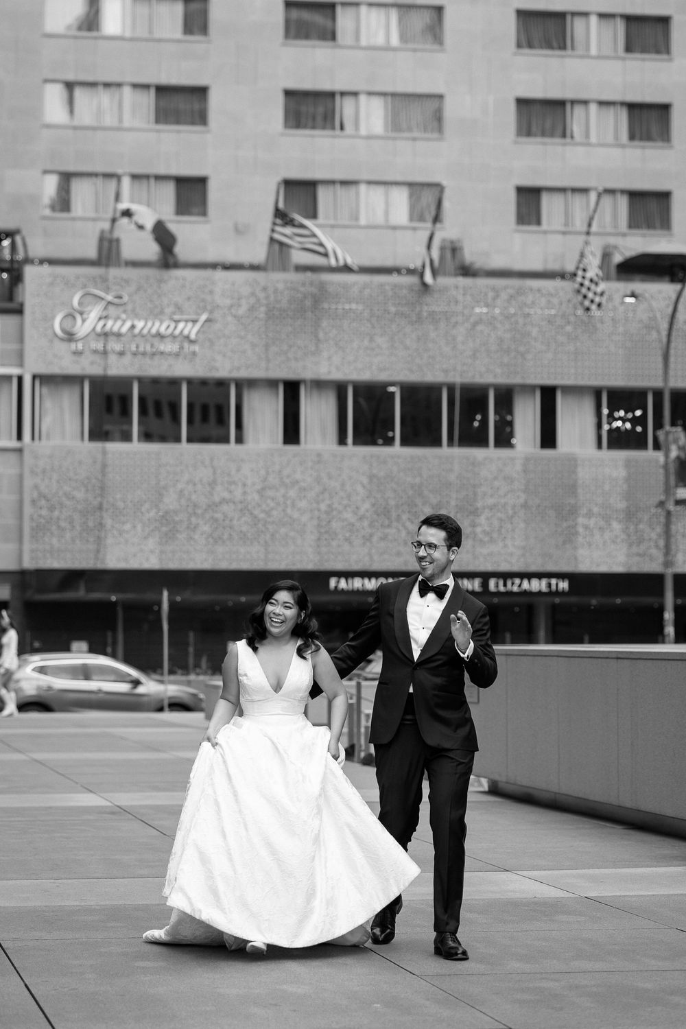 Bride and groom walk hand in hand outside the Fairmont Queen Elizabeth hotel in black and white.  Captured by Montreal wedding photographer.