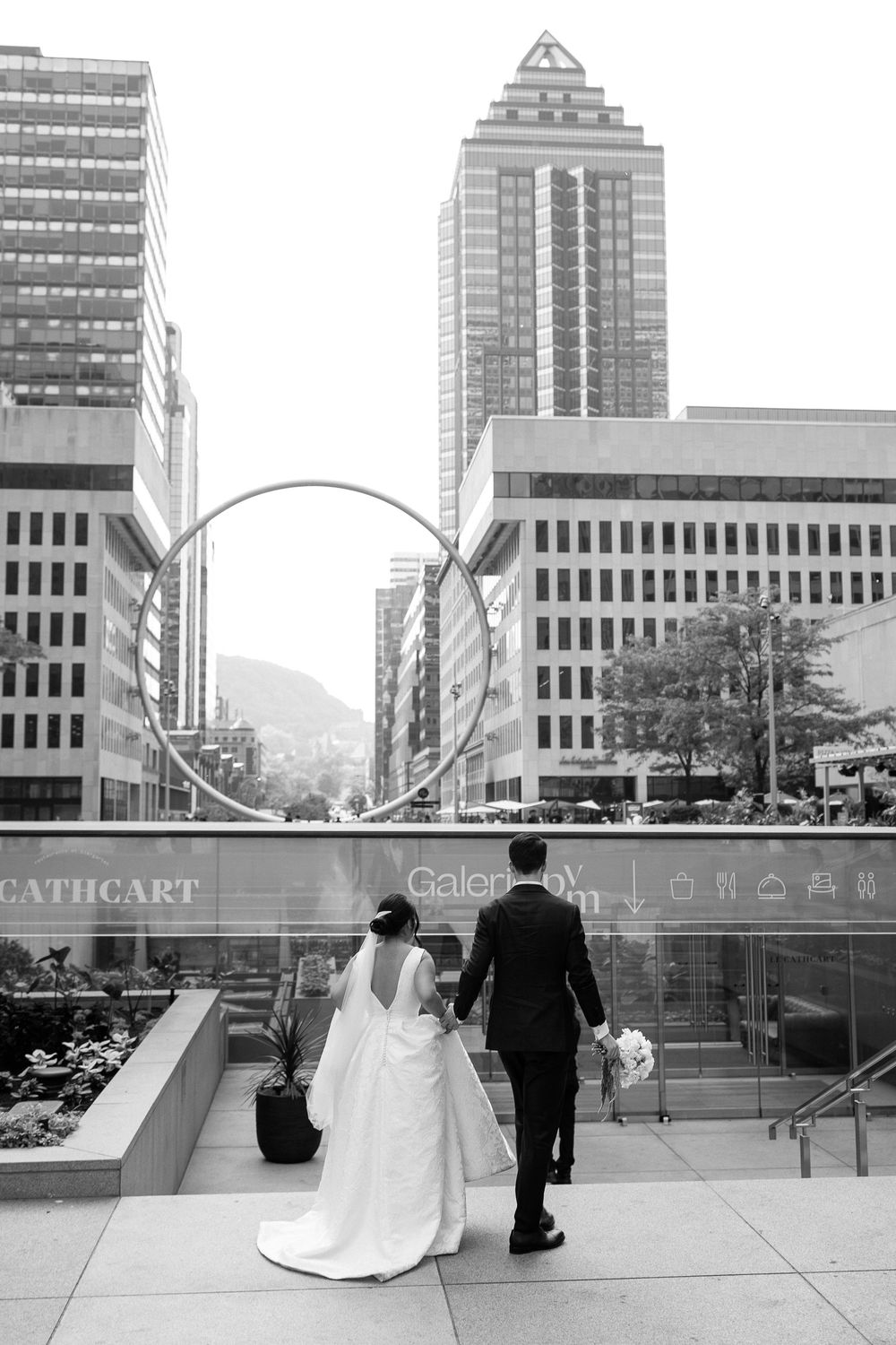 Bride and groom walk hand-in-hand into Le Cathcart wedding venue with skyscrapers in front of them, captured in black and white.