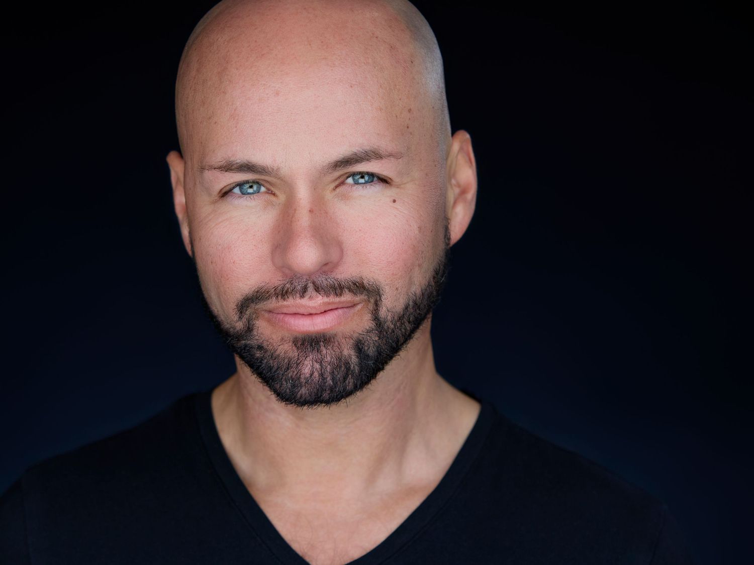 Professional headshot of a bald man with blue eyes and beard wearing a black v-neck shirt.