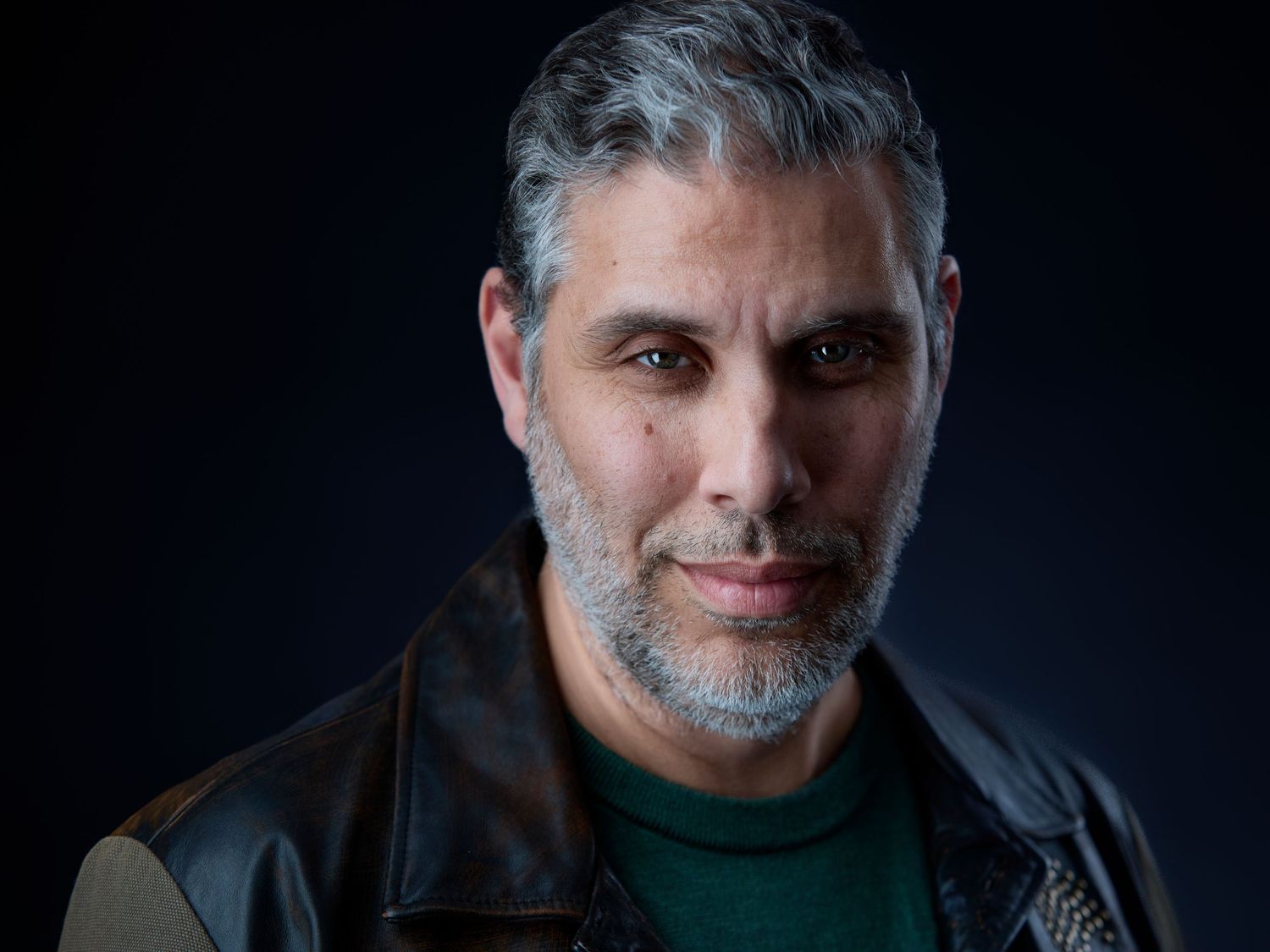 Professional headshot of a middle-aged man with gray hair and beard wearing a leather jacket.