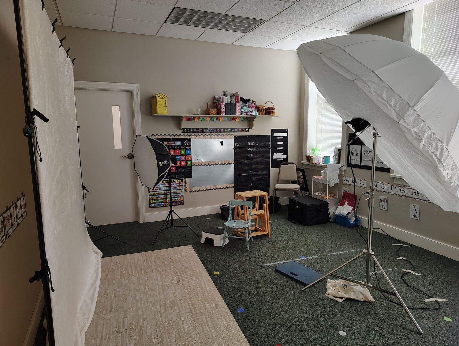 Professional photography studio setup with lighting equipment, umbrellas, and backdrops in a carpeted room.