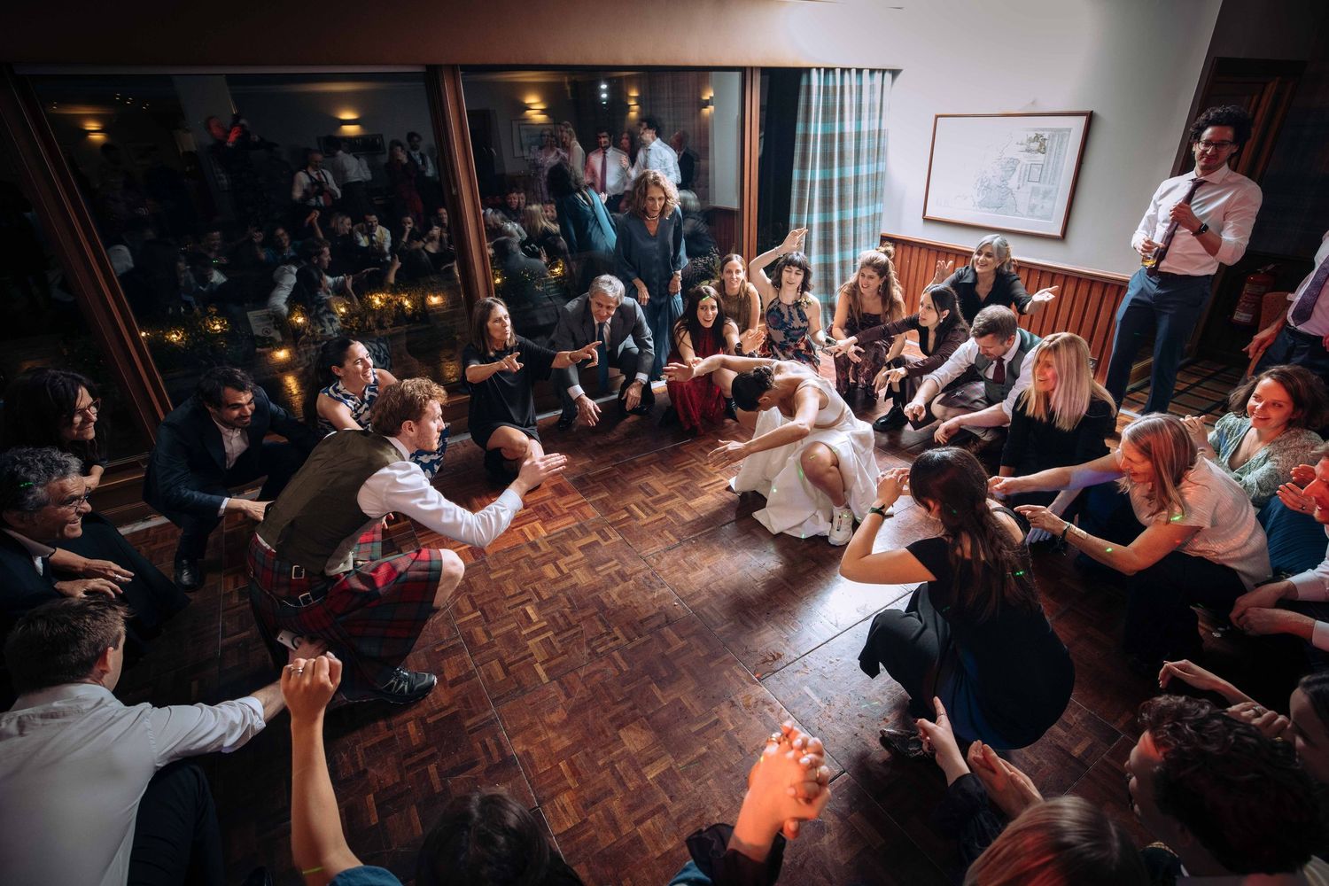 Large group of people sitting in a circle on a wooden dance floor at a lively indoor social gathering.