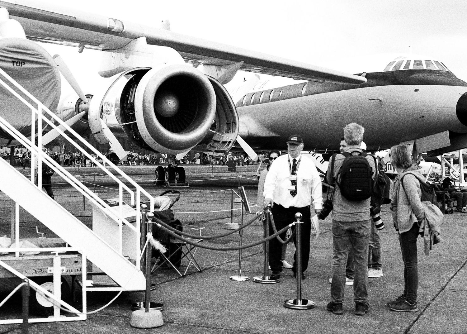 Visitors examine a large commercial jet aircraft engine up close at an outdoor airshow event.