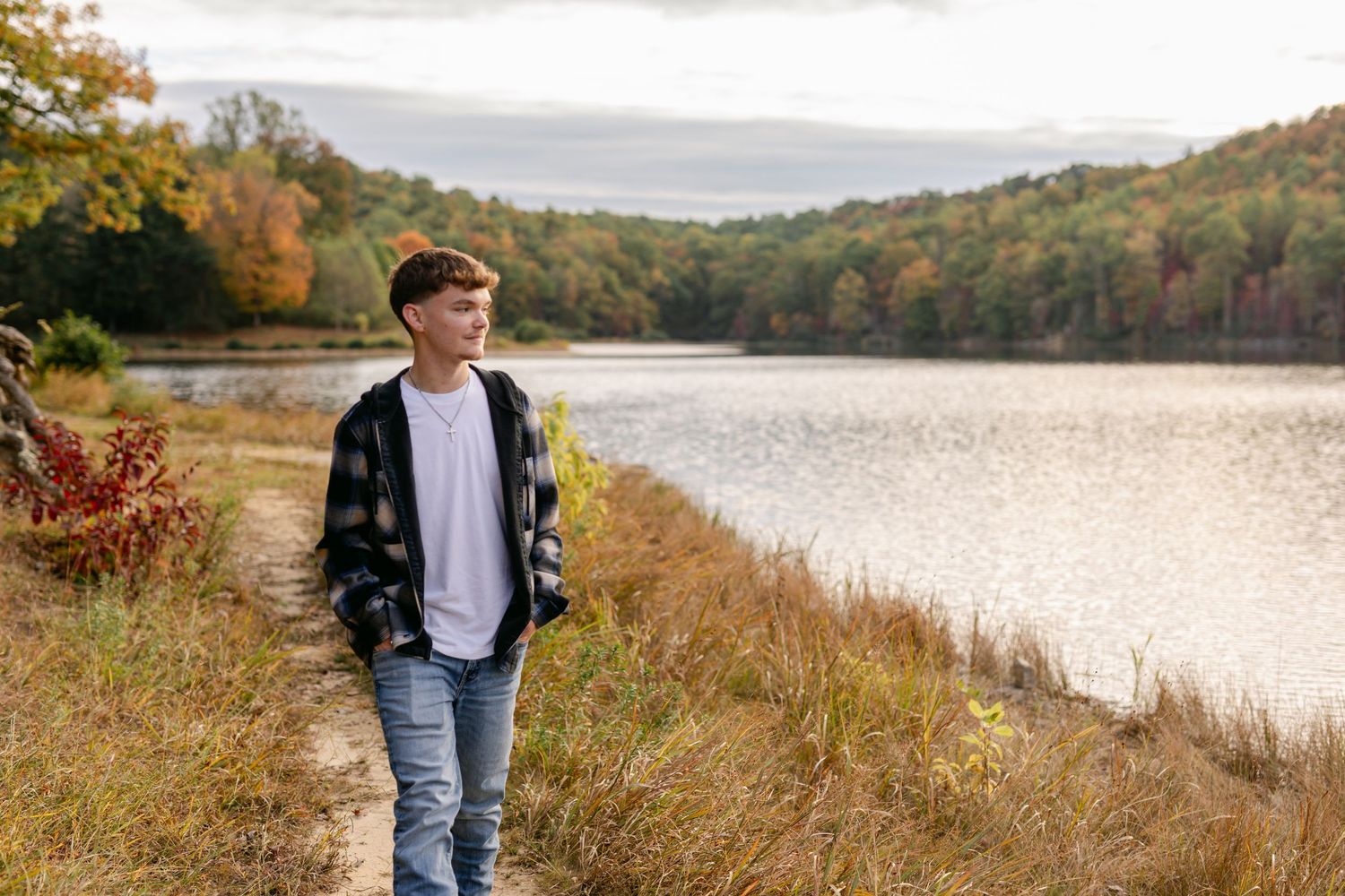 Young man in flannel shirt standing by scenic autumn lake with colorful foliage.