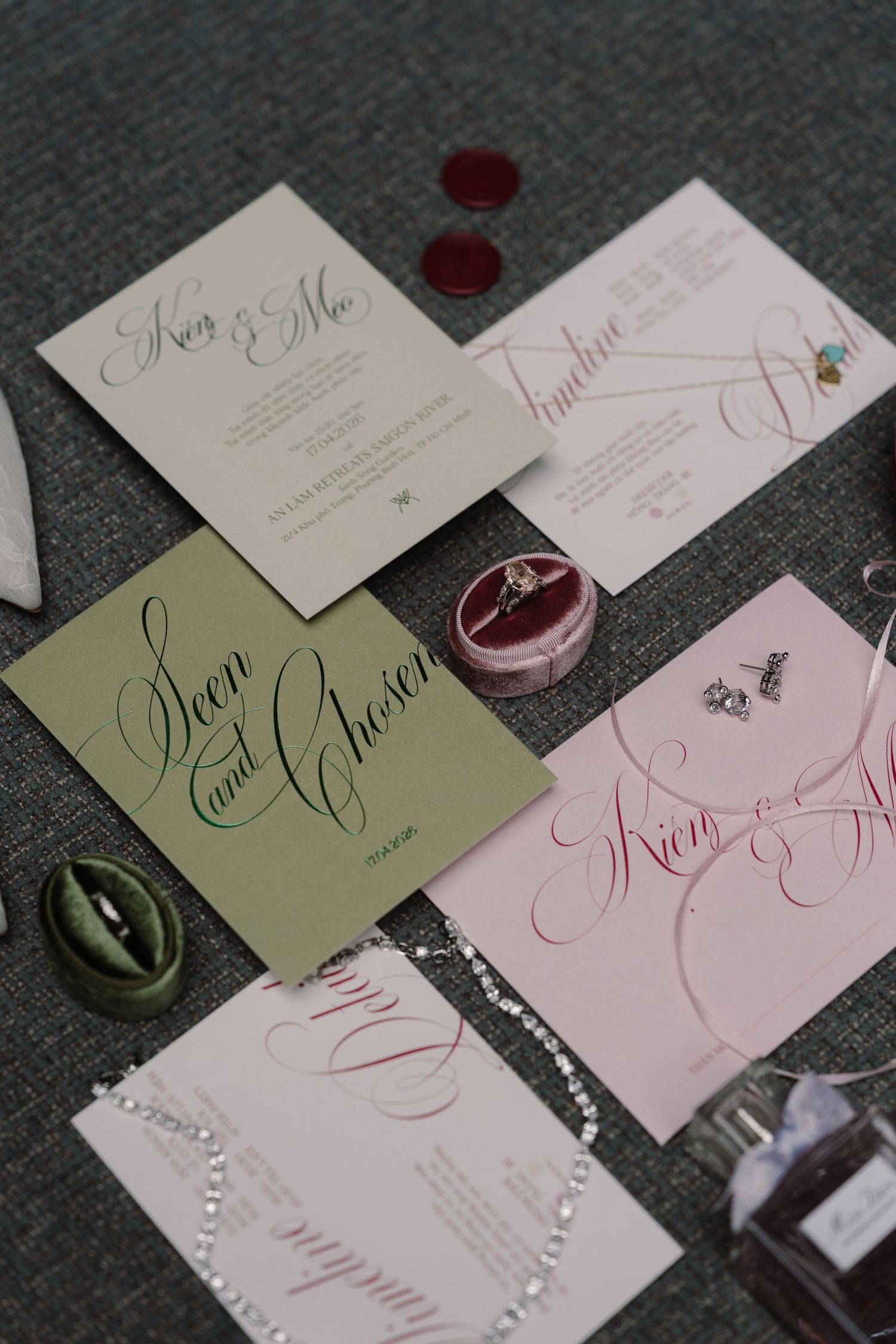 Elegant wedding stationery flat lay featuring pink and sage green calligraphy cards with velvet ring box and accessories.