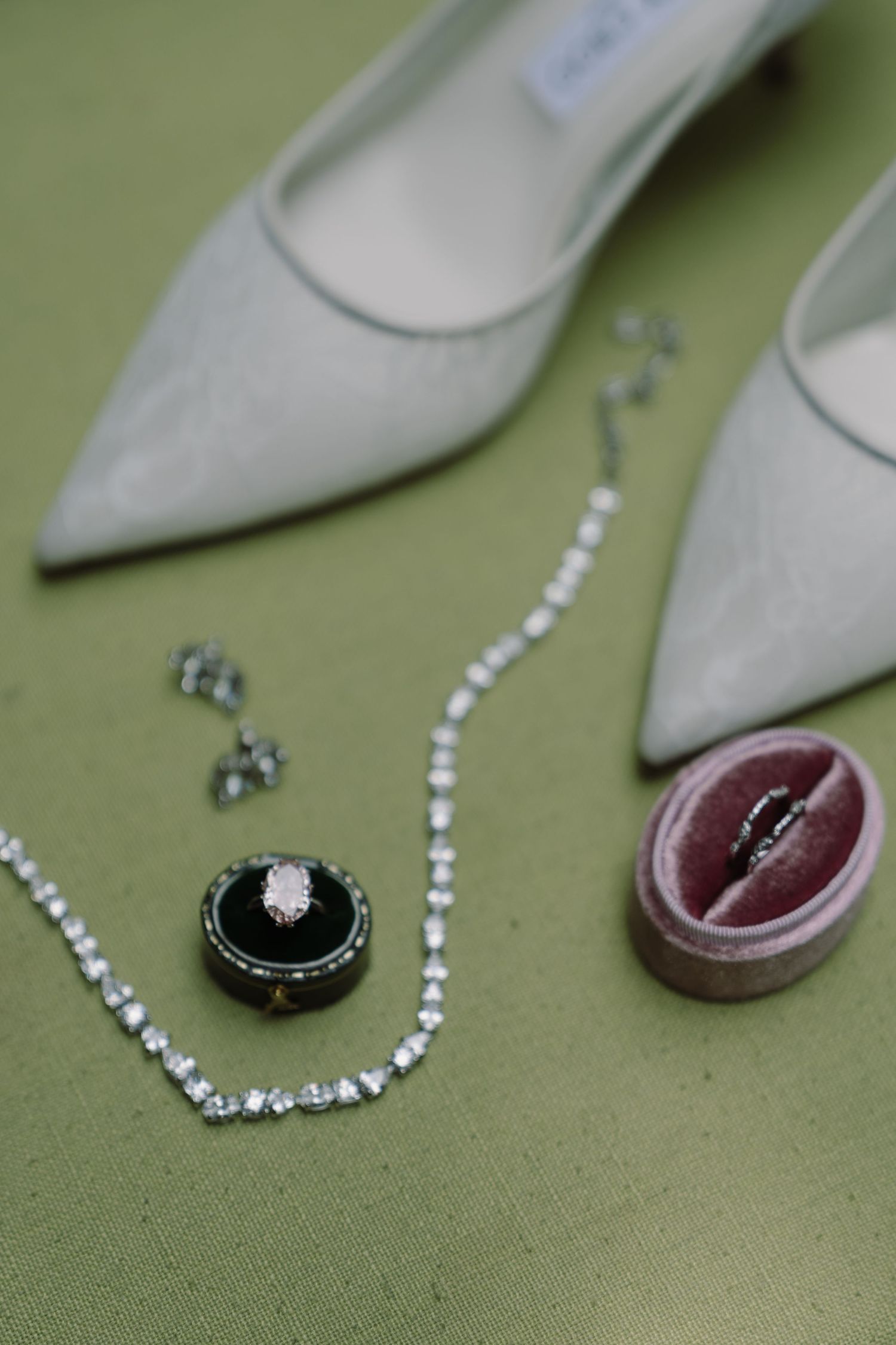 Wedding flat lay featuring diamond ring, necklace, earrings, and silver Jimmy Choo heels on green.