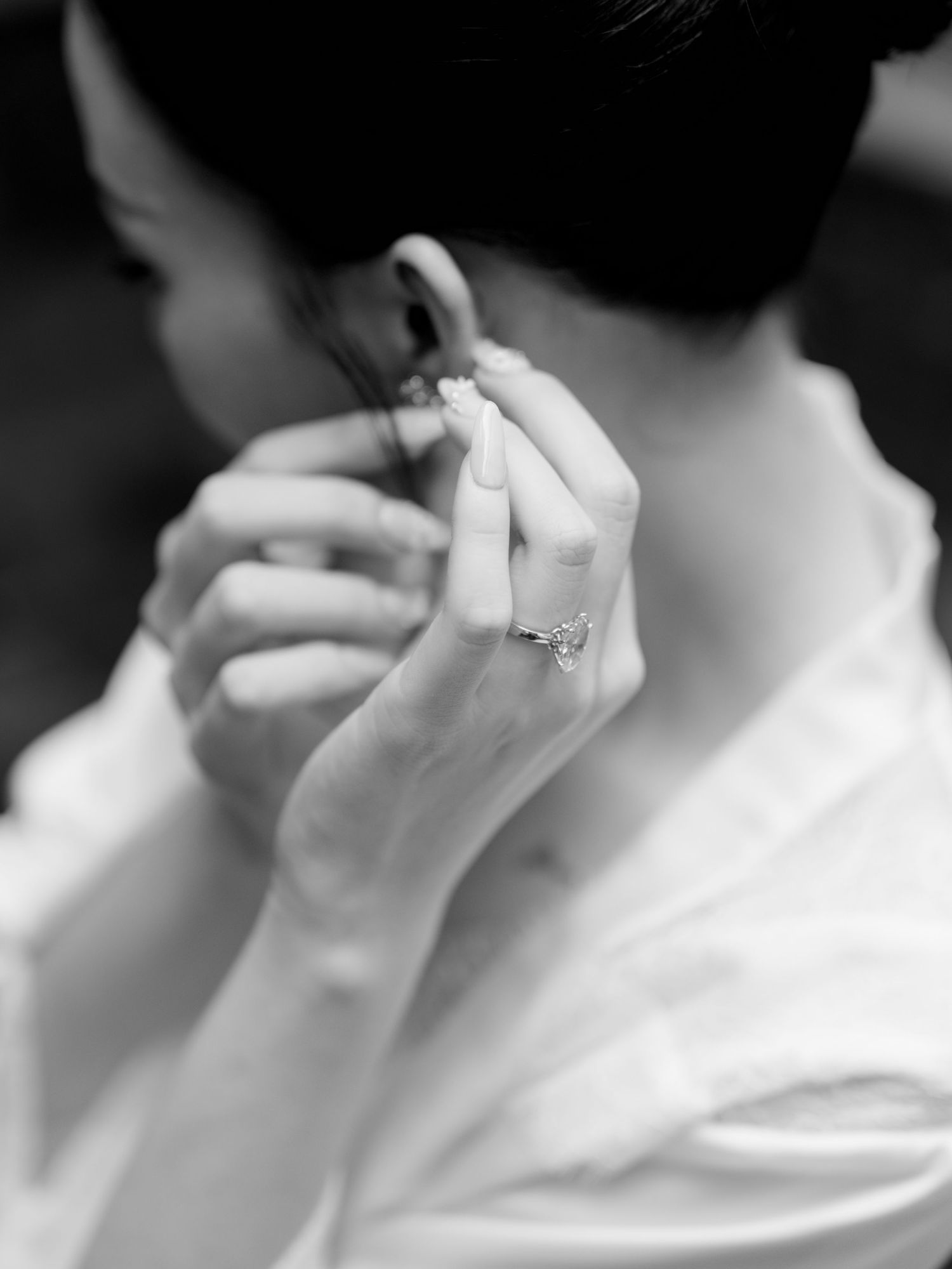 Black and white close-up of bride adjusting earring wearing diamond engagement ring on wedding day.