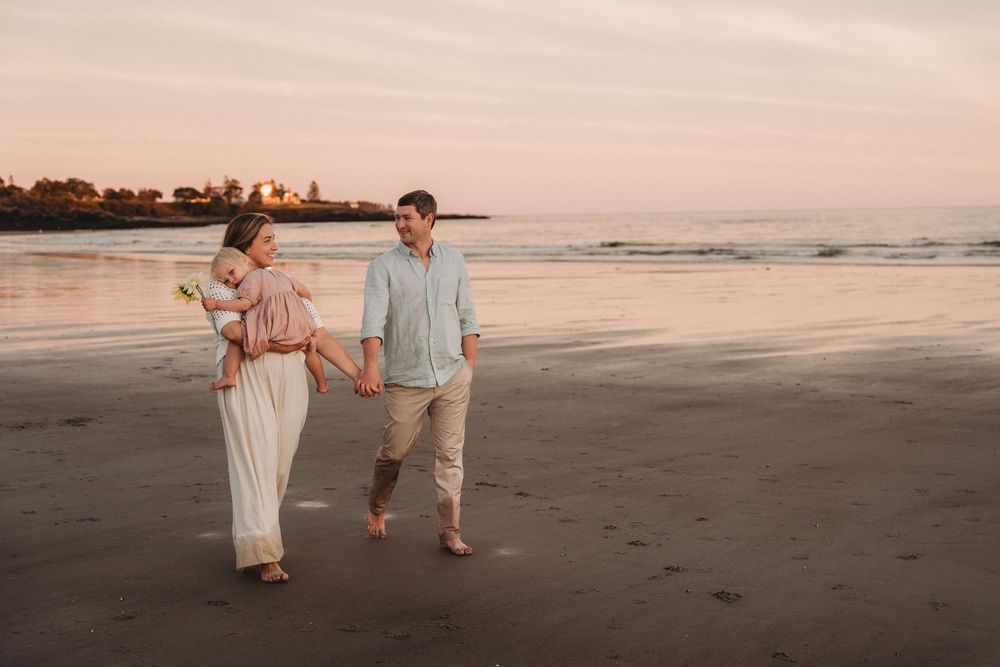 Couple walking hand-in-hand on a sandy beach at sunset, woman in white dress, man in light blue shirt.