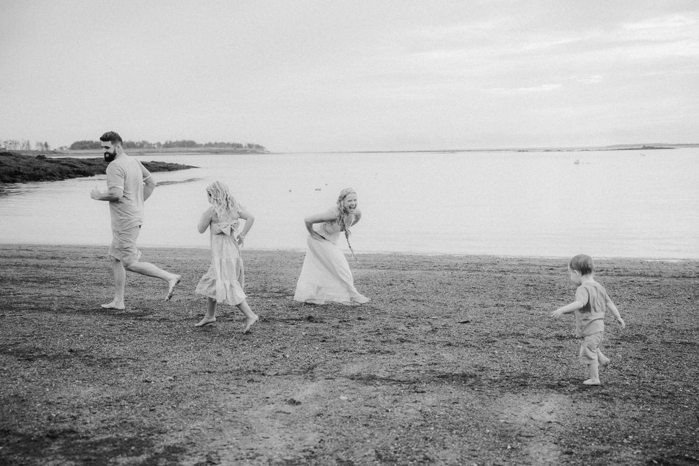 Black and white photo of a family walking along a beach shoreline, with two adults and two children enjoying a casual stroll.