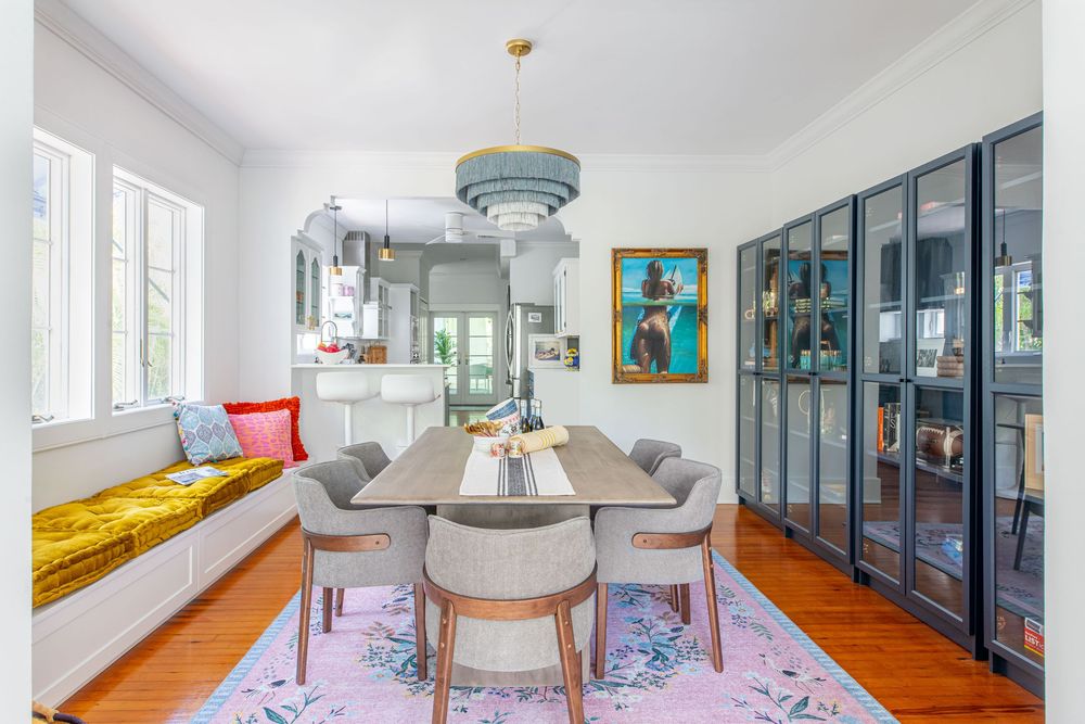 Modern dining room with gray chairs, wood table, pink rug, built-in bench, blue chandelier, and dark glass cabinet.