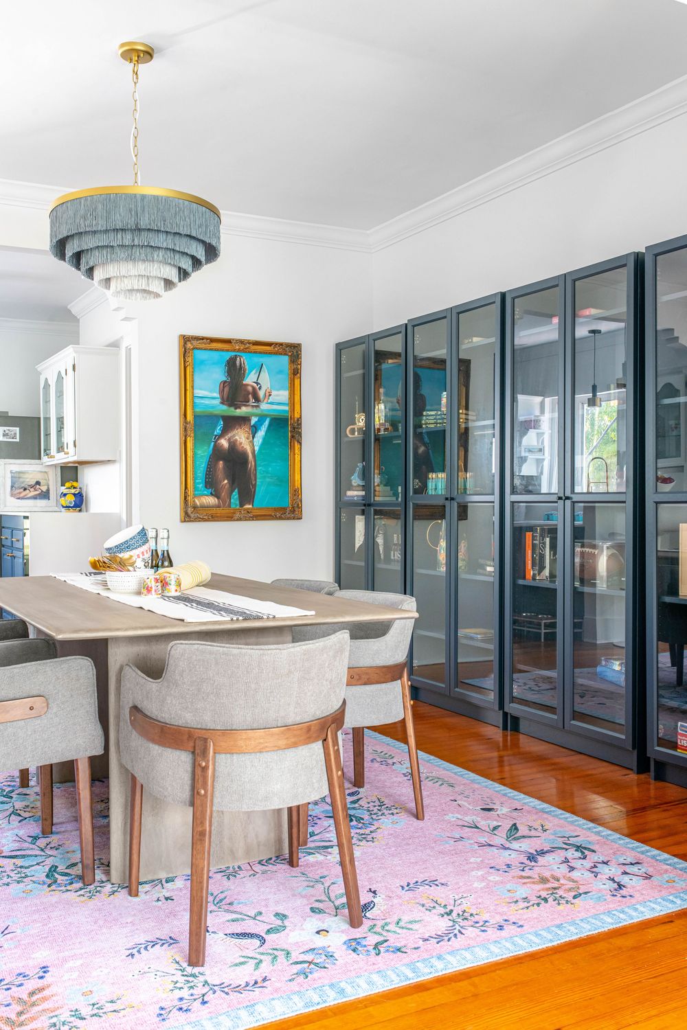 Eclectic dining room with gray chairs, wood table, pink floral rug, dark cabinet wall unit, and fringe chandelier.