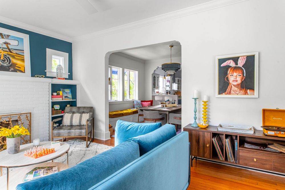 Eclectic living room with teal blue sofa, hardwood floors, teal accent wall, and colorful artwork in a bright home.