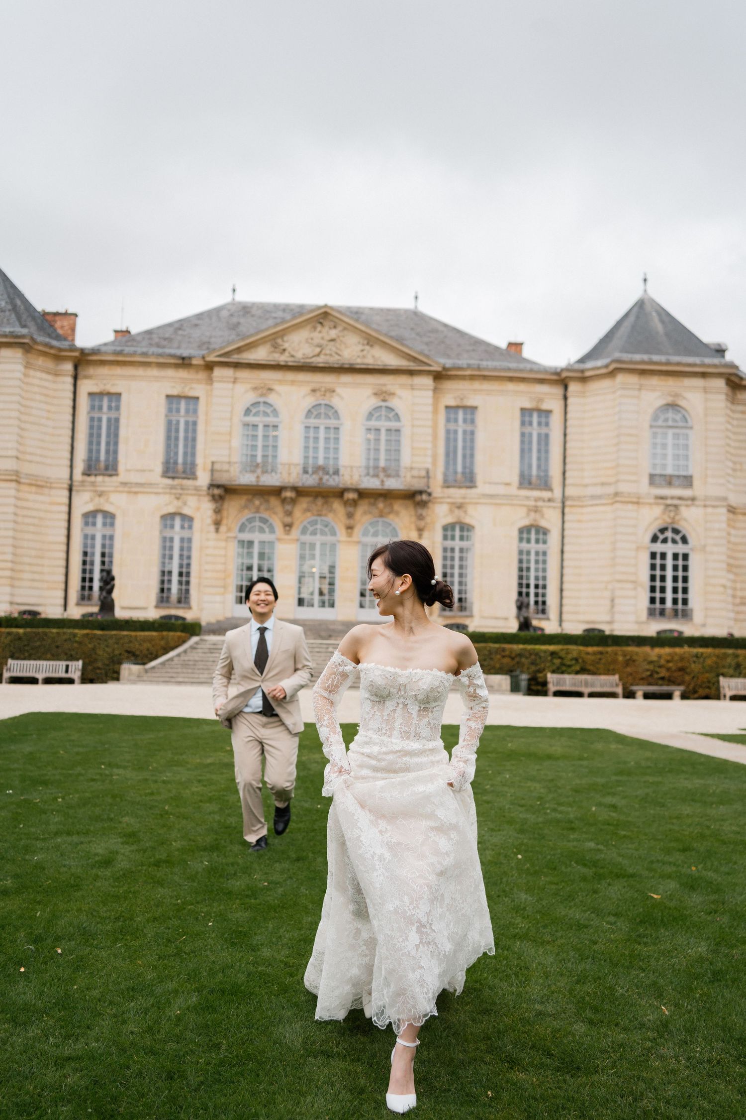 Bride and groom running on green lawn before elegant French chateau on cloudy day in Paris. Elopement photography paris, film