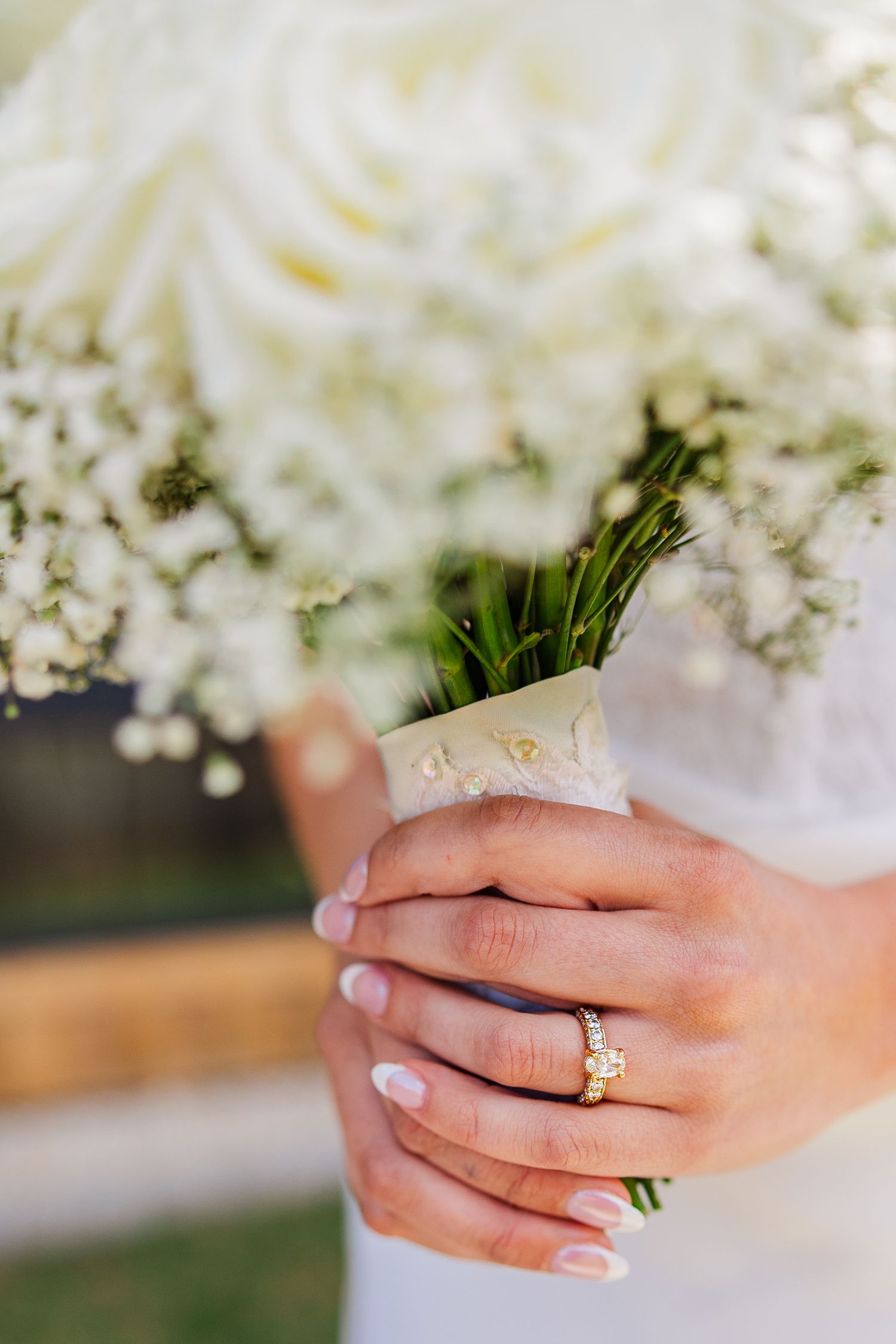 Bride holding white rose and baby's breath bouquet with diamond engagement ring and gold wedding band.