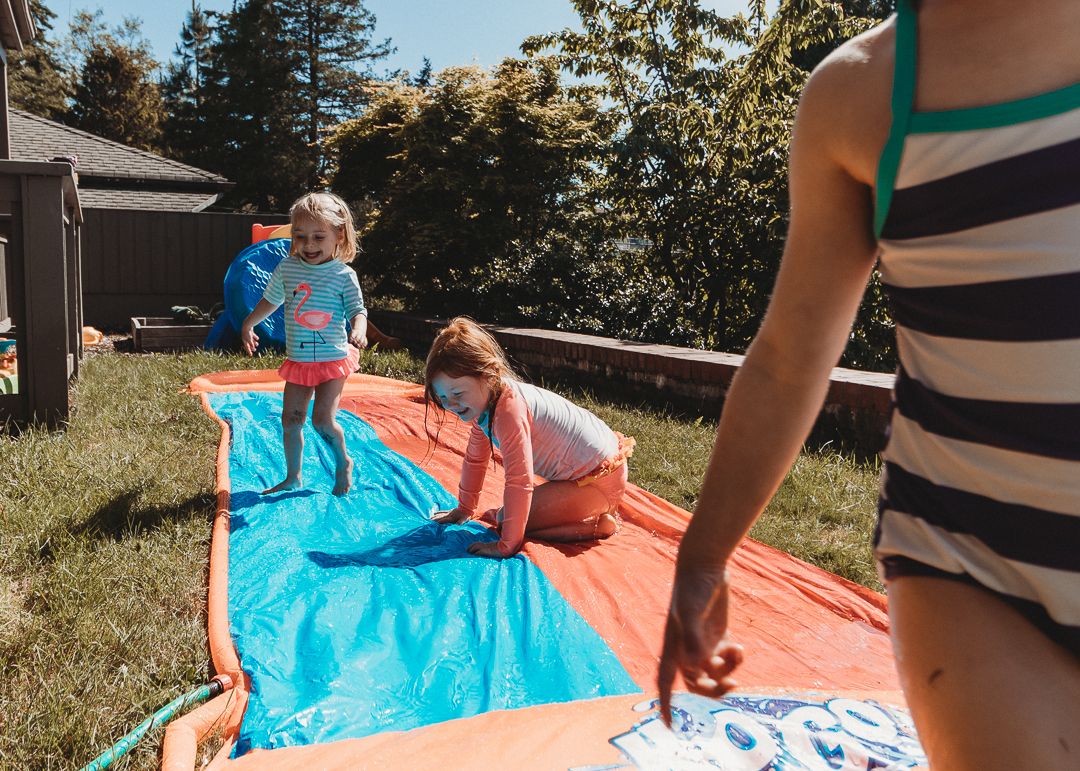 Two children playing on a backyard slip and slide on a sunny summer day.