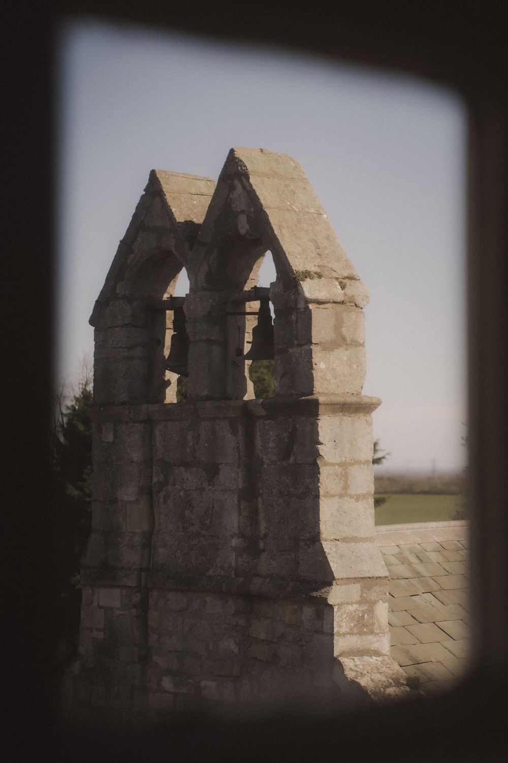 Ancient stone bell tower with Gothic arches viewed through a window frame, set against a clear sky.