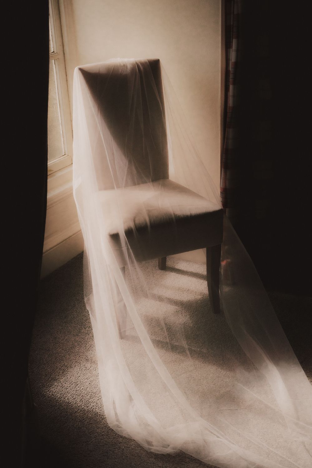 A bridal veil draped elegantly over a chair near a softly lit window in a dimly lit room.