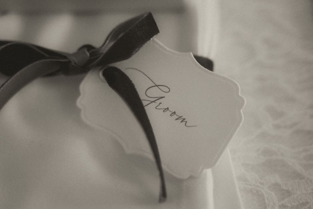 Elegant black and white wedding groom gift tag with ribbon bow on lace fabric.