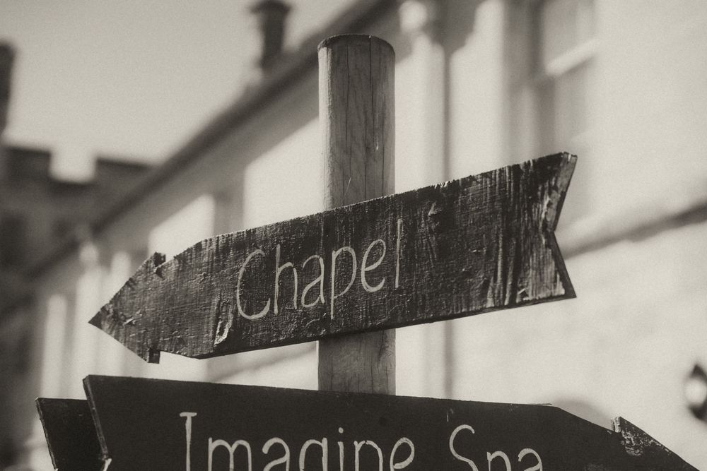 Vintage wooden directional signs pointing to Chapel and Imagine Spa in black and white photography.