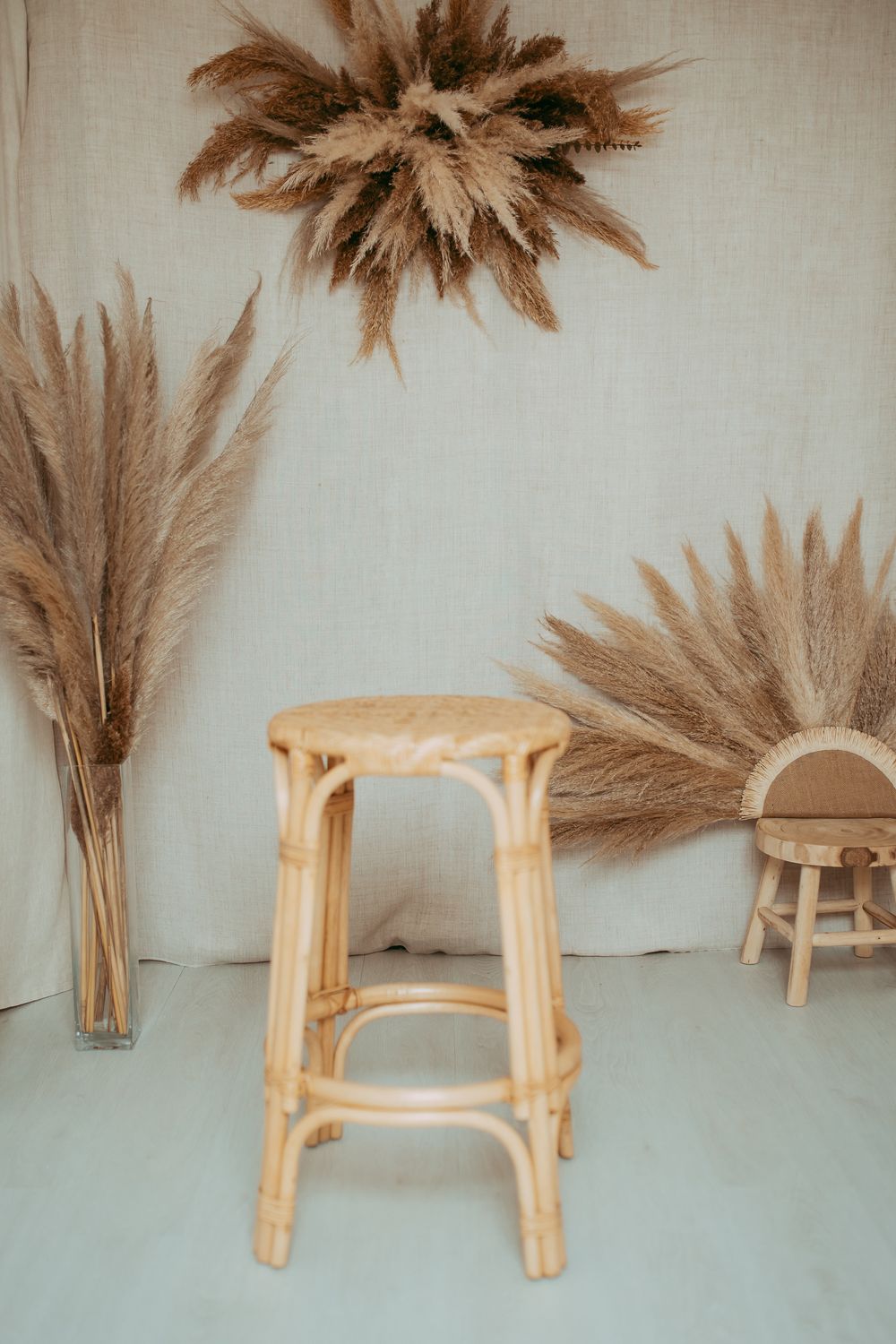 Boho-style rattan stool surrounded by dried pampas grass arrangements against a neutral linen backdrop.