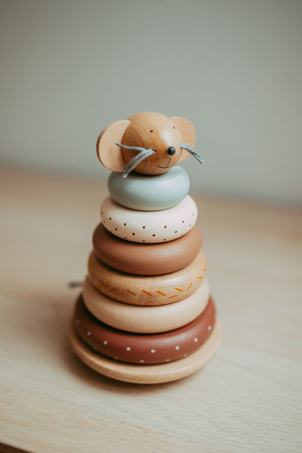 Wooden stacking toy with mouse topper and colorful rings in neutral tones on a light wood surface.