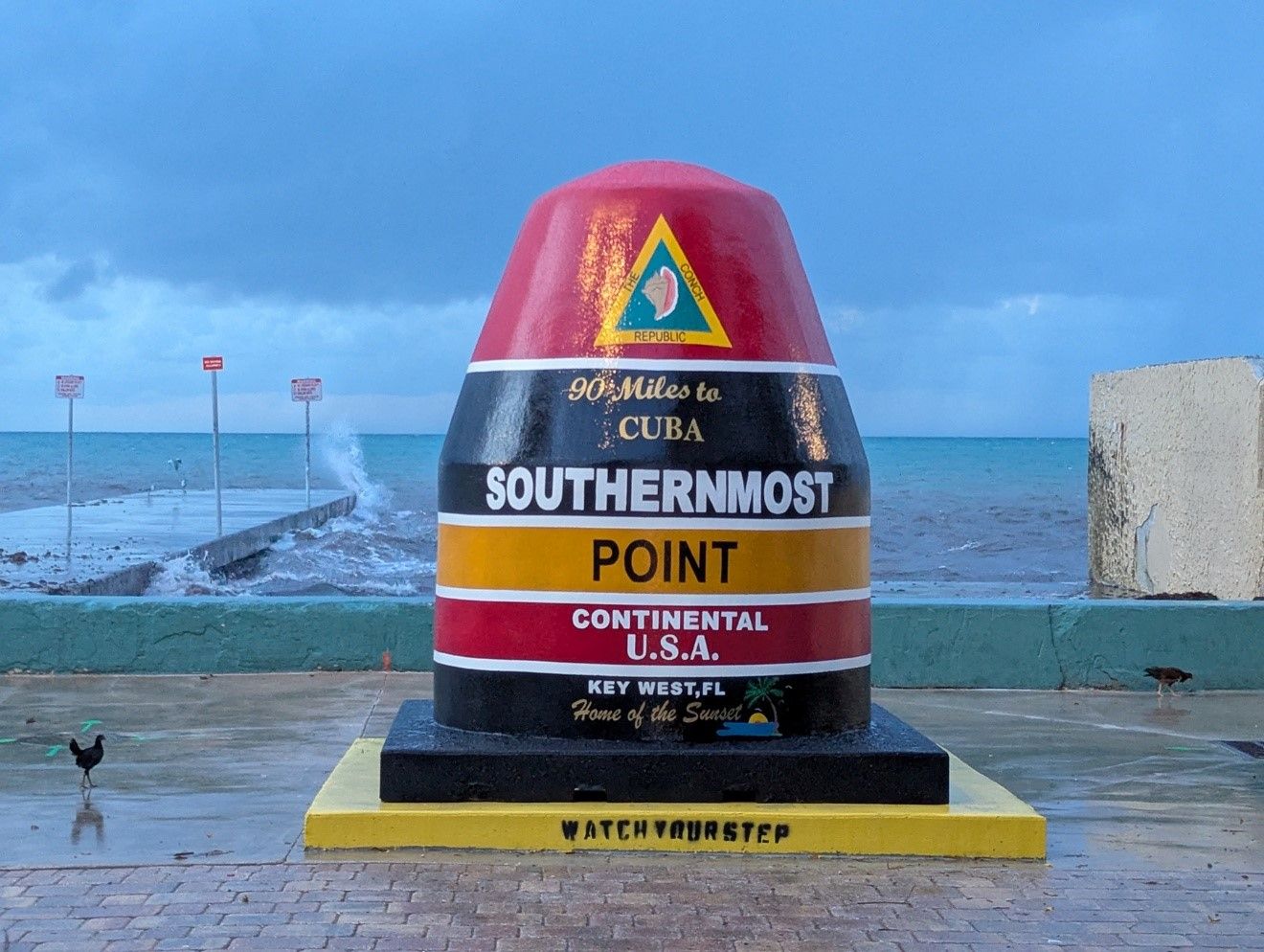 The iconic Southernmost Point buoy monument in Key West, Florida, marking 90 miles to Cuba on a cloudy day.