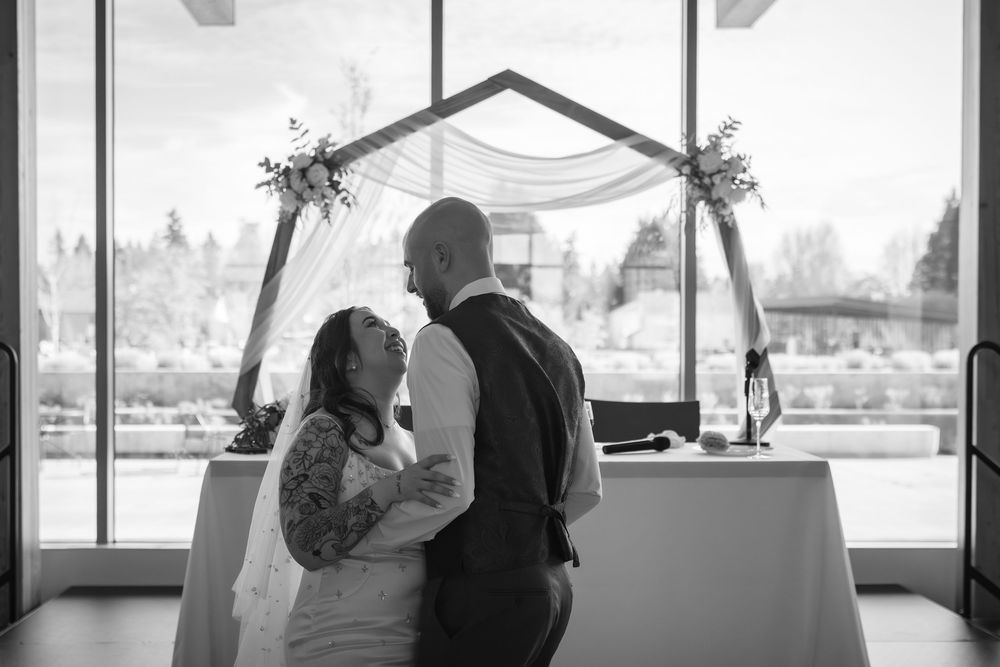 Black and white silhouette of bride and groom at altar with hexagonal arch and flowers.