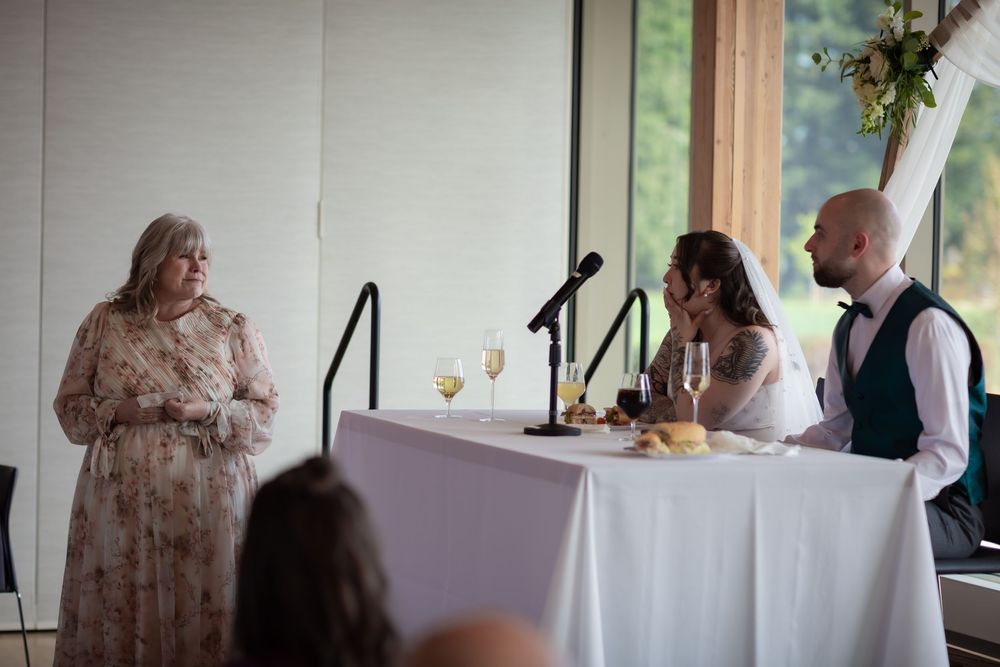 Guest giving a toast speech to bride and groom at wedding reception dinner table.