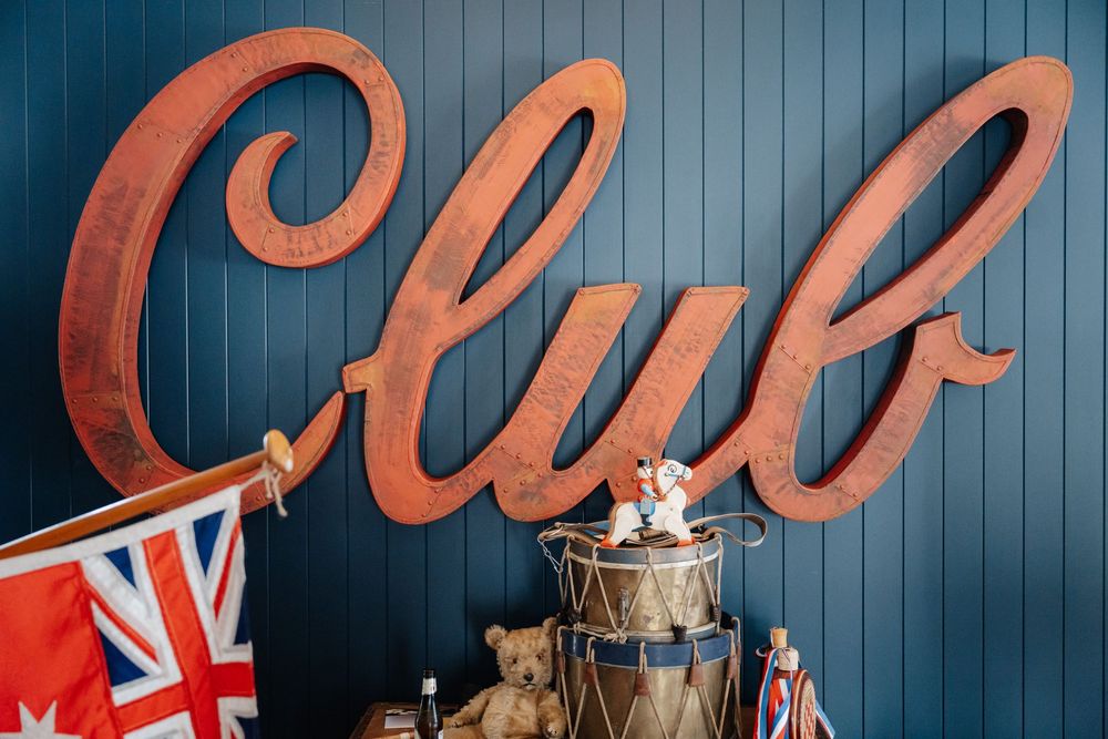 Rustic metal Club sign on blue wall with Union Jack flags and vintage teddy bear decorations.