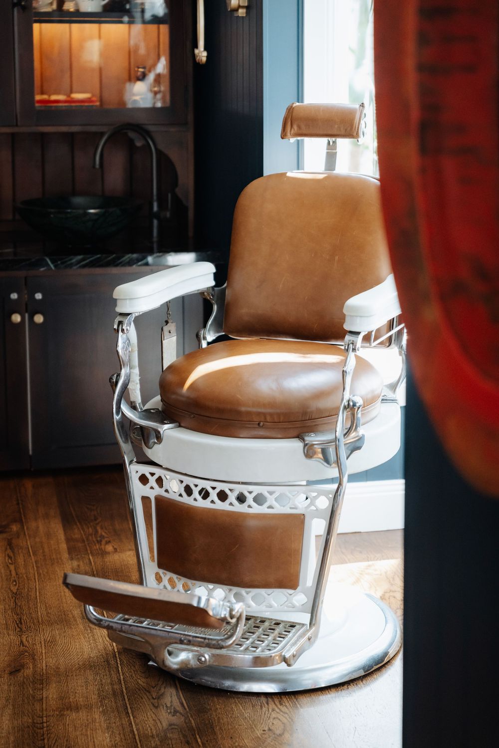 Vintage brown leather barber chair with chrome details on hardwood floor in a classic barbershop interior.