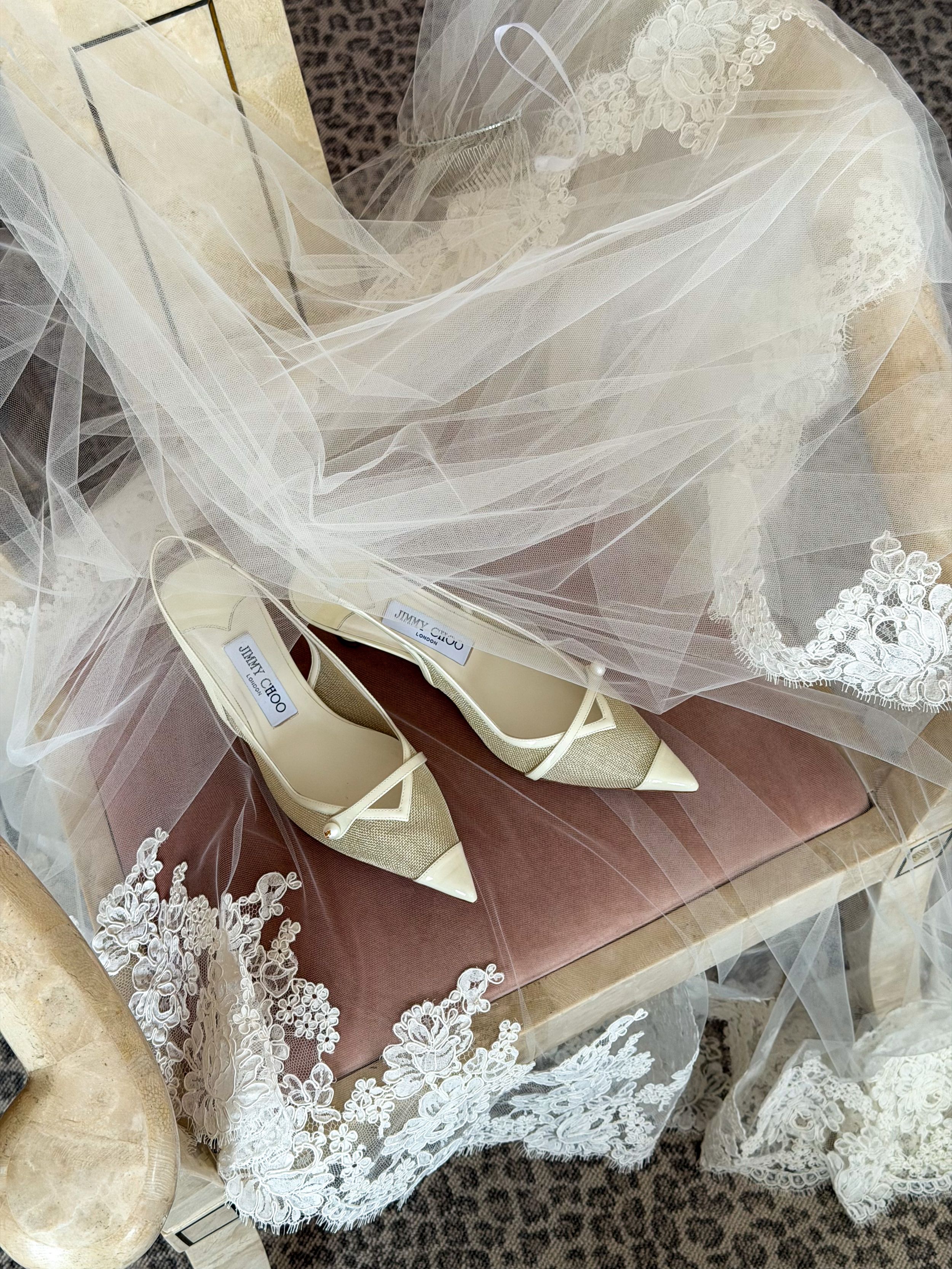 Ivory Jimmy Choo bridal heels resting on pink velvet beside a lace-trimmed wedding veil.
