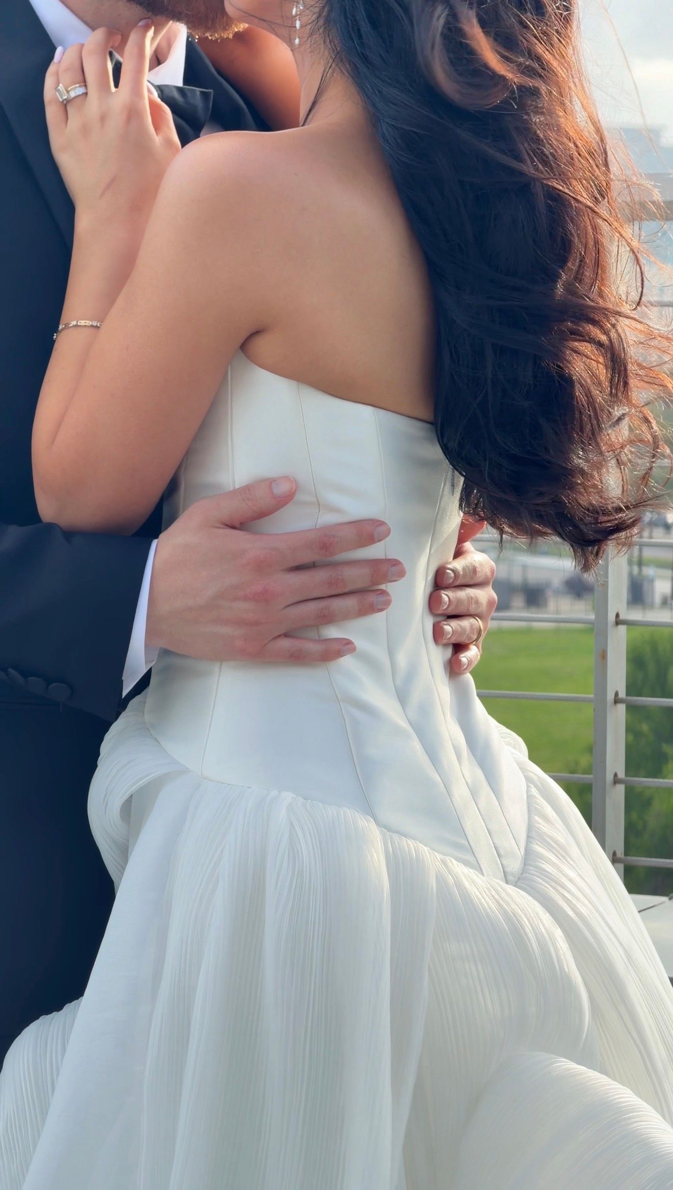 Bride in strapless white corset gown embracing groom, showcasing back detail and flowing skirt.