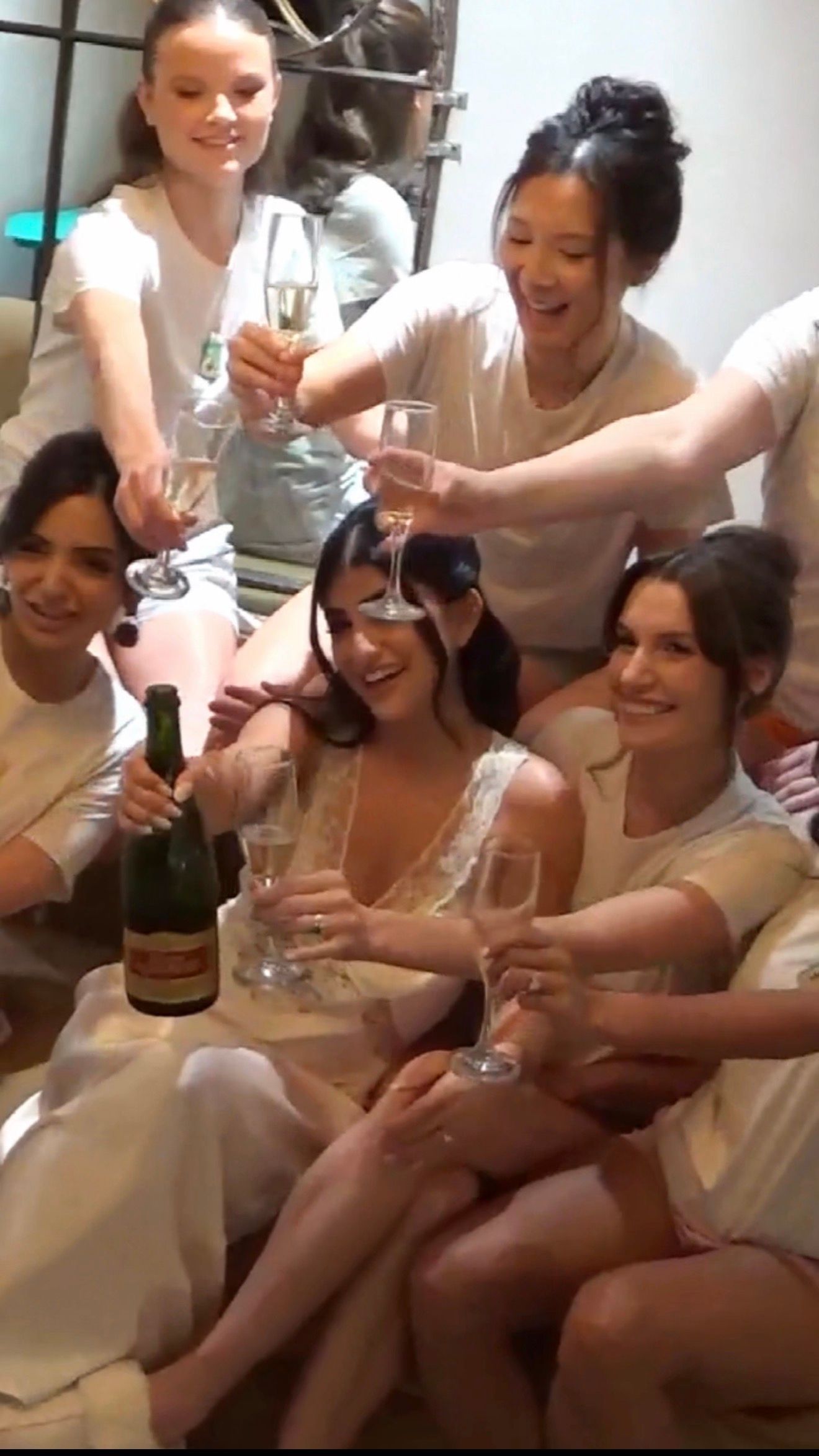 Group of bridesmaids in white robes celebrating with champagne glasses before a wedding ceremony.