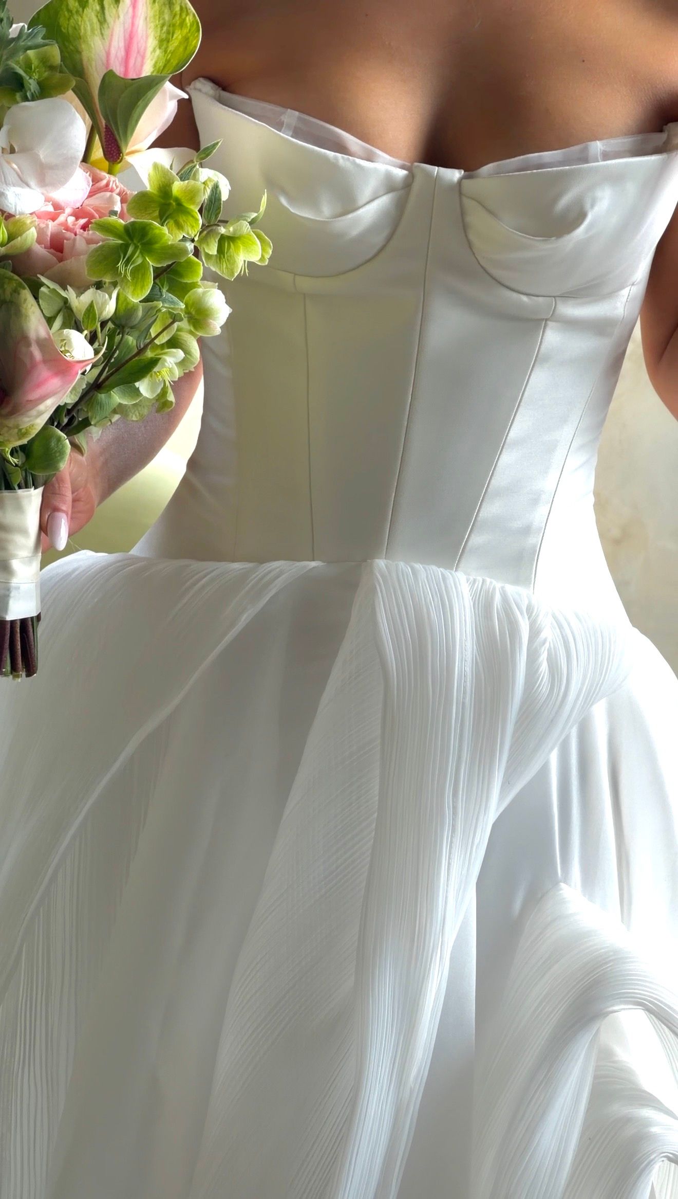 Close-up of a bride in a white strapless corset wedding gown holding a pink and green floral bouquet.
