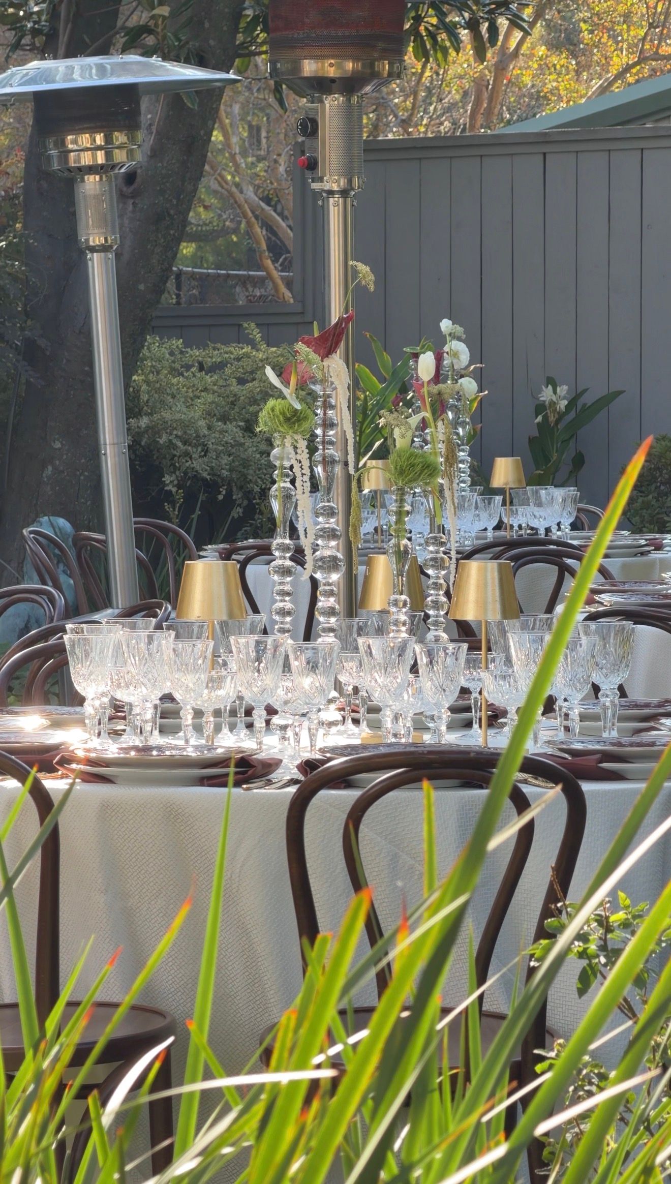 Elegant outdoor dining table set with crystal glassware, candelabras, and floral centerpieces in a garden setting.
