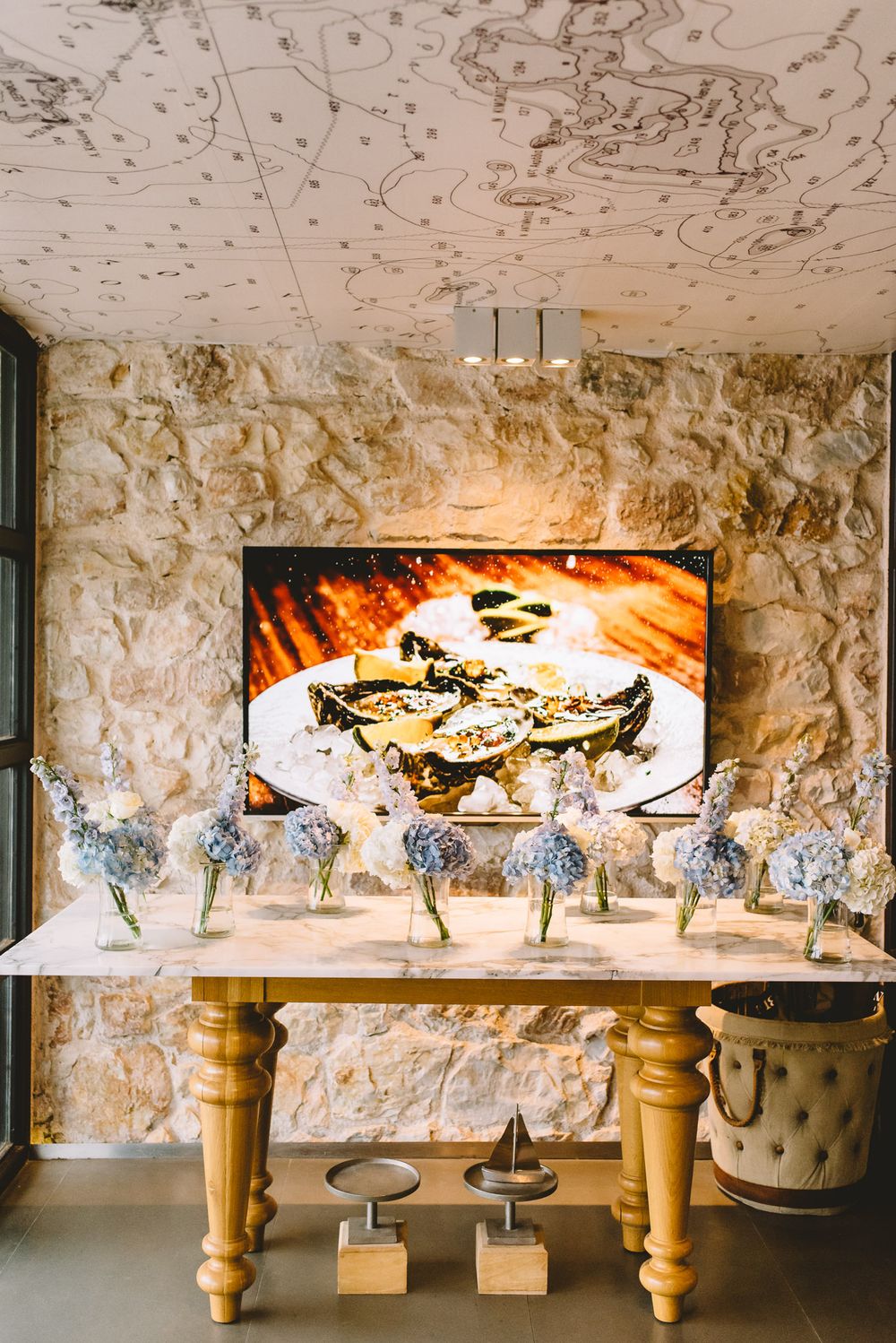 Elegant marble table with blue hydrangea arrangements, stone wall, oyster artwork, and celestial map ceiling decor.