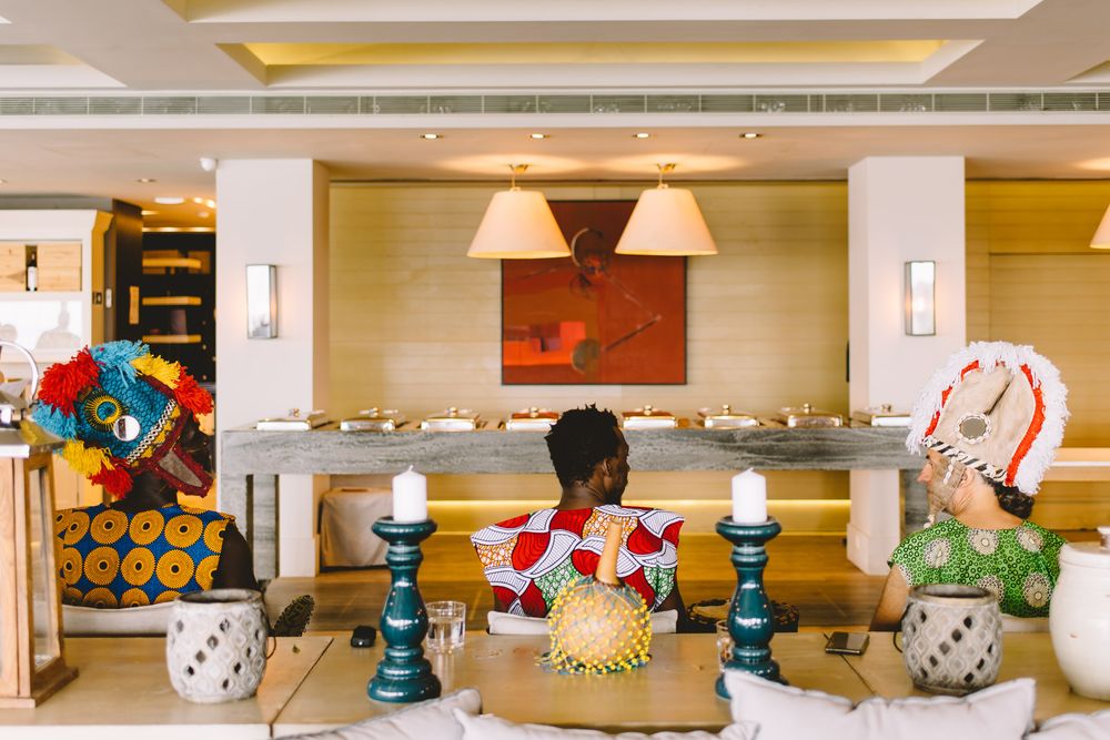 Three people in colorful African attire sit in an elegant hotel lobby with warm lighting and modern decor.