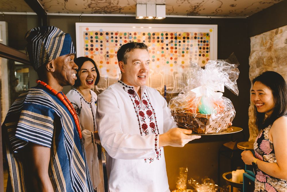 Four people in traditional attire laughing together while receiving a decorative gift basket at a festive cultural celebration.
