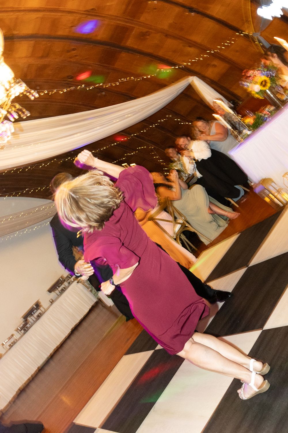 Guests dancing on a checkered dance floor at a wedding reception with string lights and draped fabric decor.