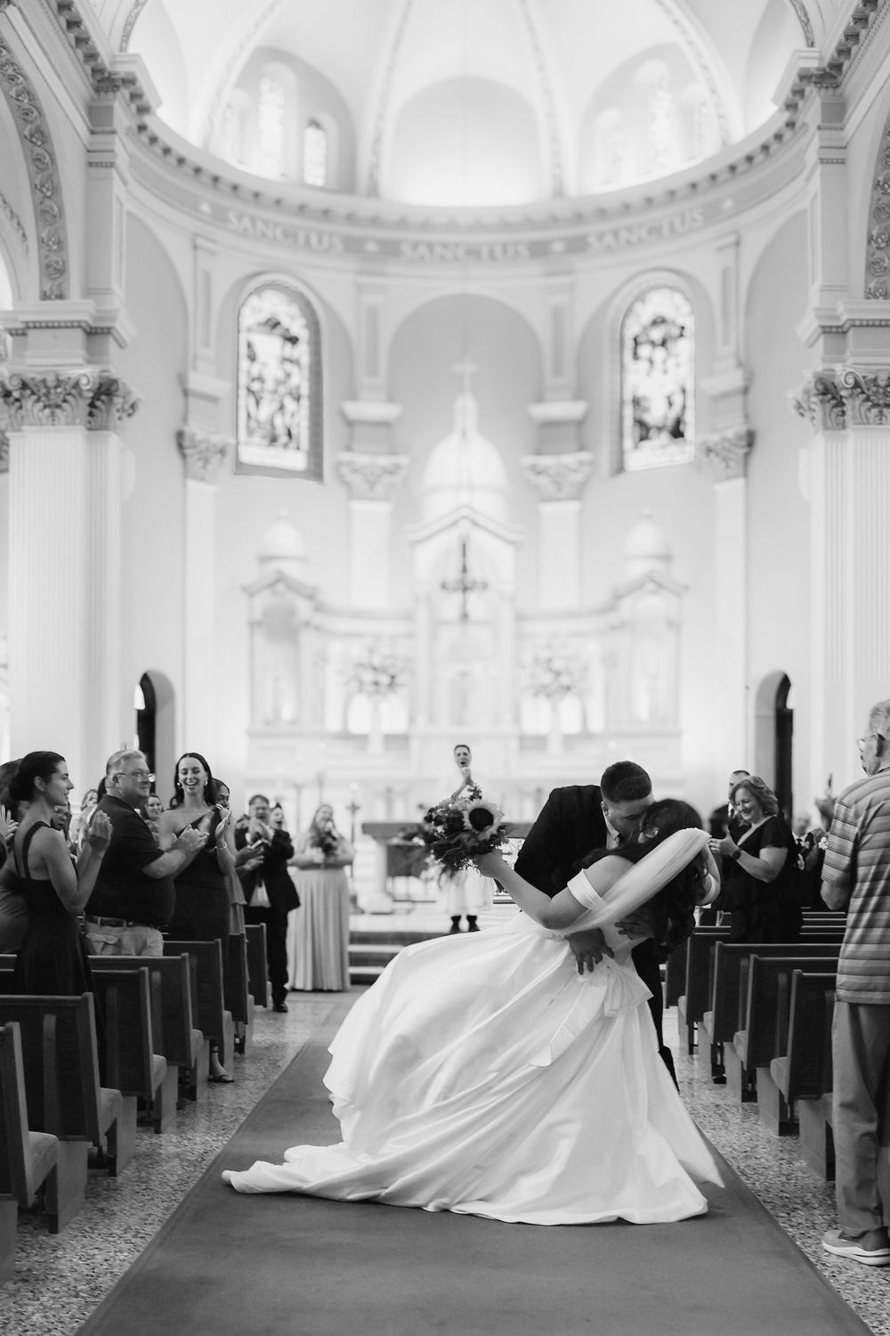 Bride and groom share romantic dip kiss in stunning cathedral church aisle after wedding ceremony.