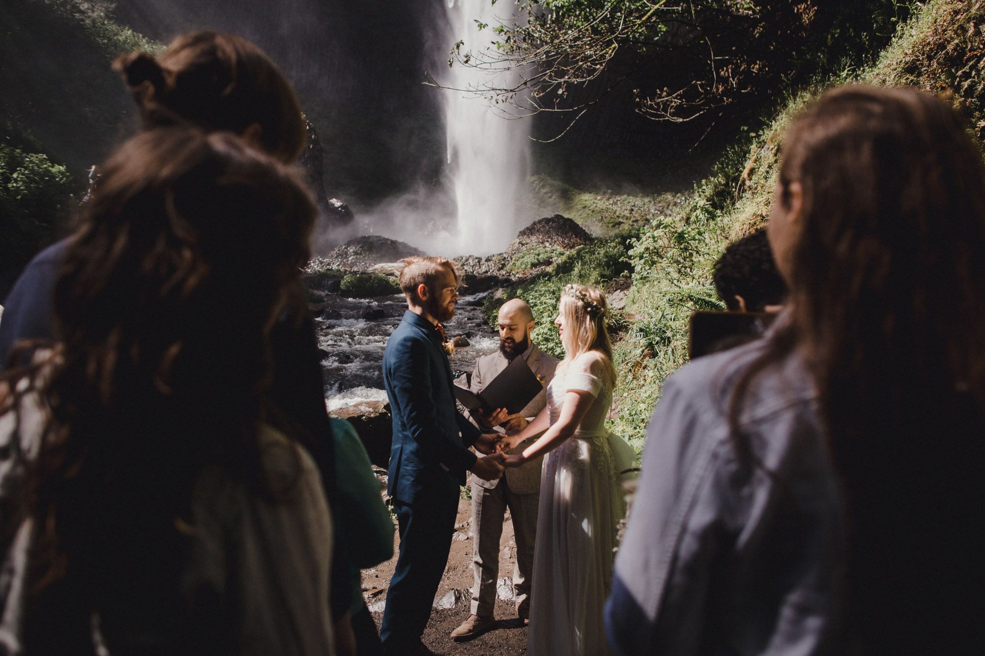 Couple exchanging vows at intimate waterfall wedding ceremony surrounded by guests at Latourell Falls in Oregon