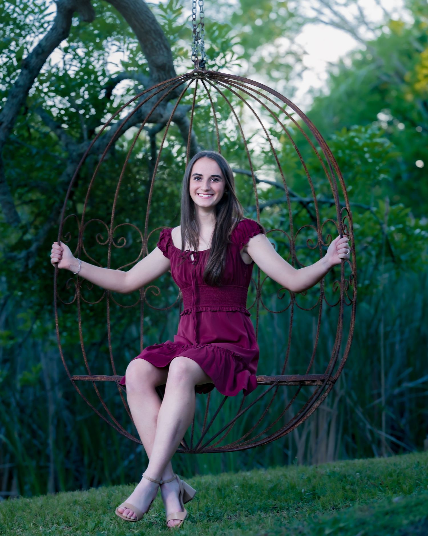 Young woman in varsity jacket and red skirt smiling by wooden fence outdoors.