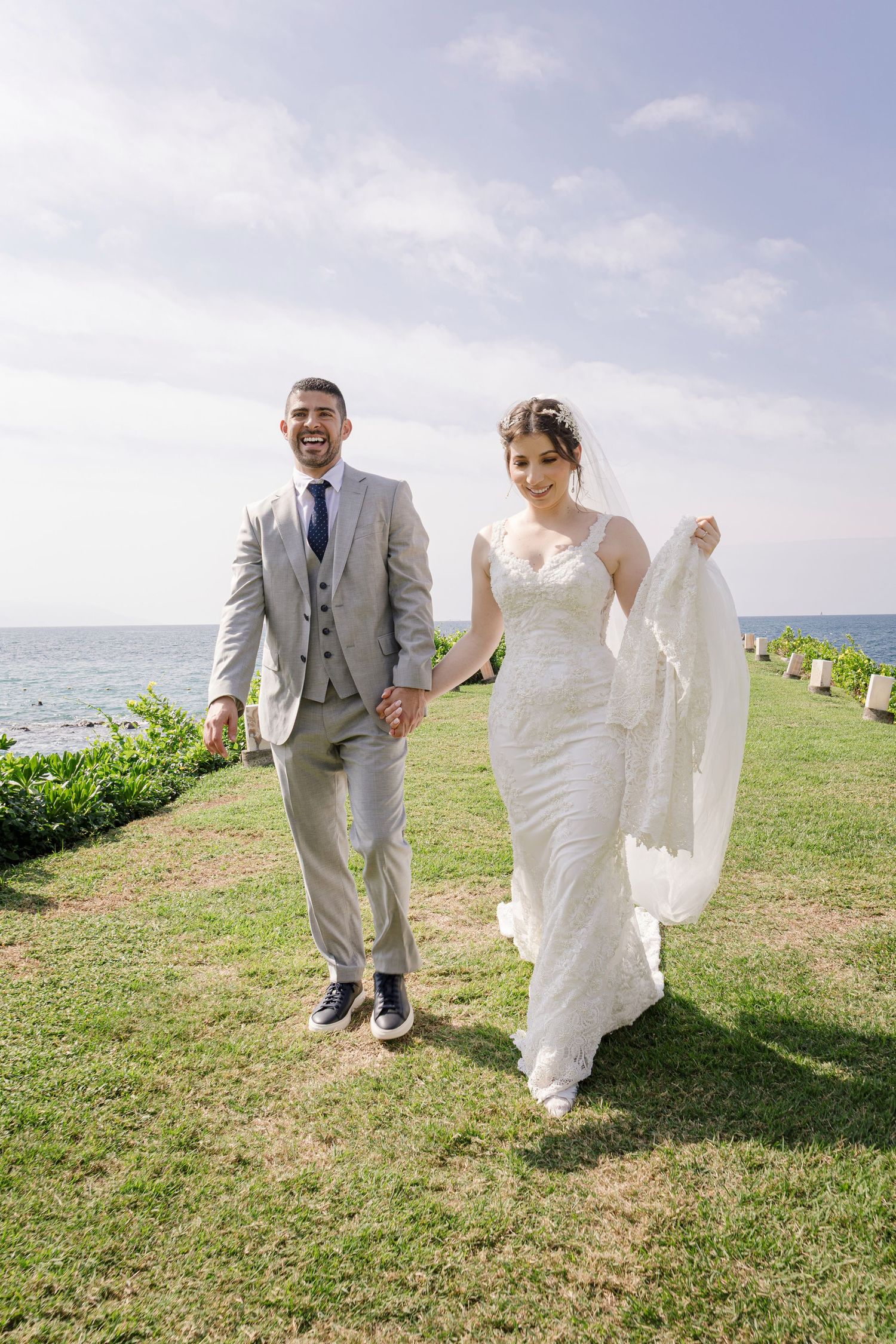 Una pareja en su boda camina por un sendero de césped frente al mar en su día especial.