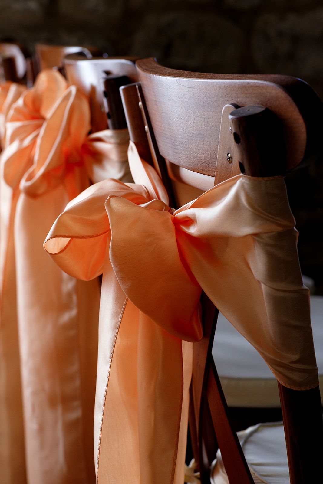 Wooden wedding chairs decorated with elegant orange satin ribbon bows, arranged in a row for a ceremony.