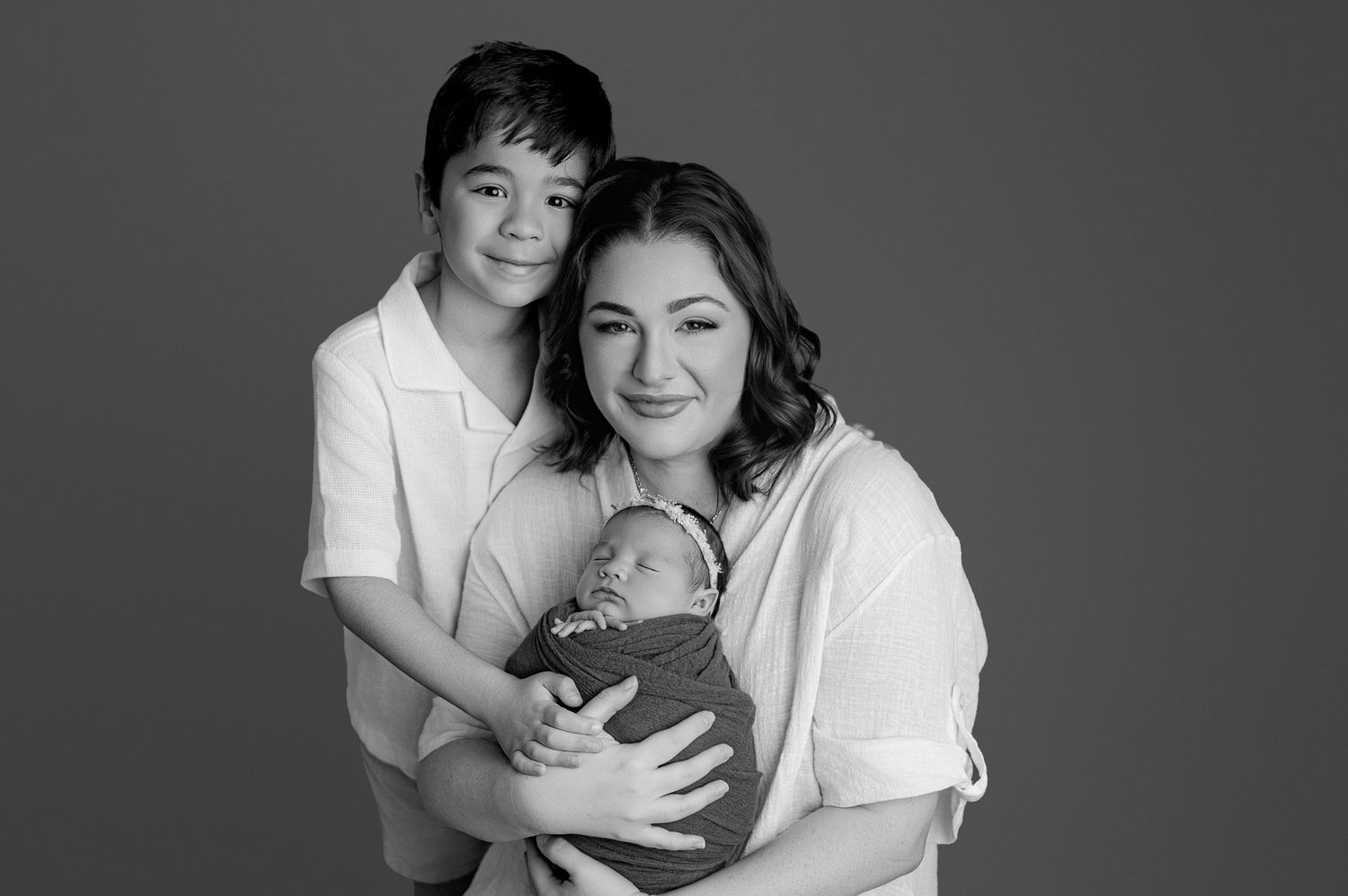 Black and white portrait of a mother holding a newborn baby with her young son beside her in a studio.