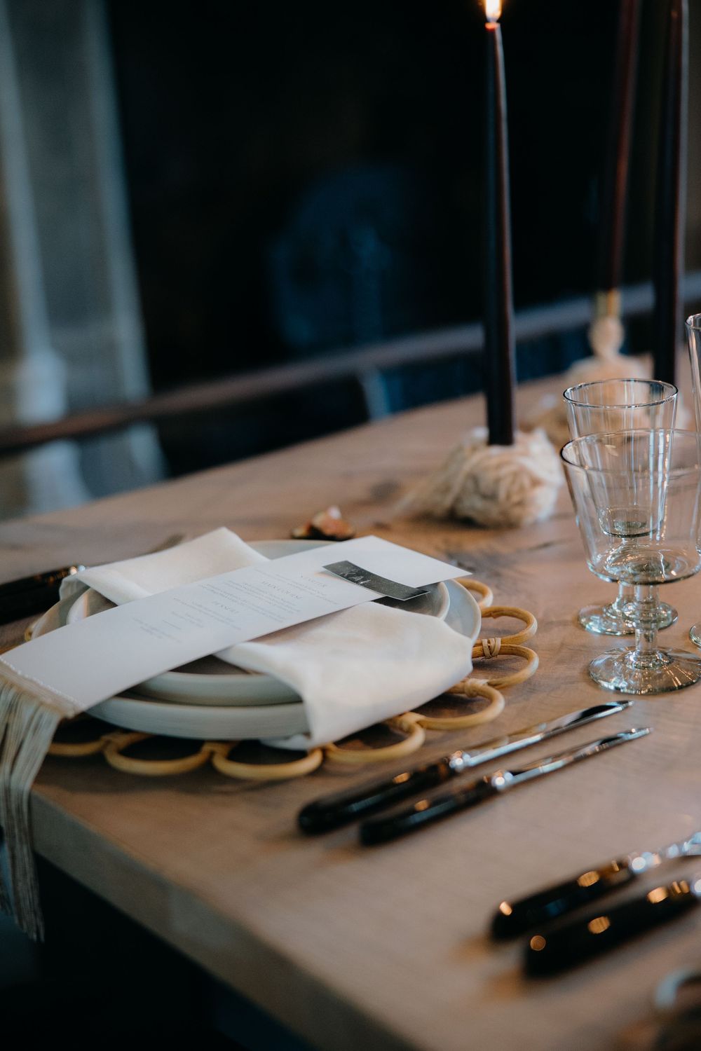 Elegant table setting with white napkin, cutlery, glass rings, candles, and crystal glasses on a wooden table.