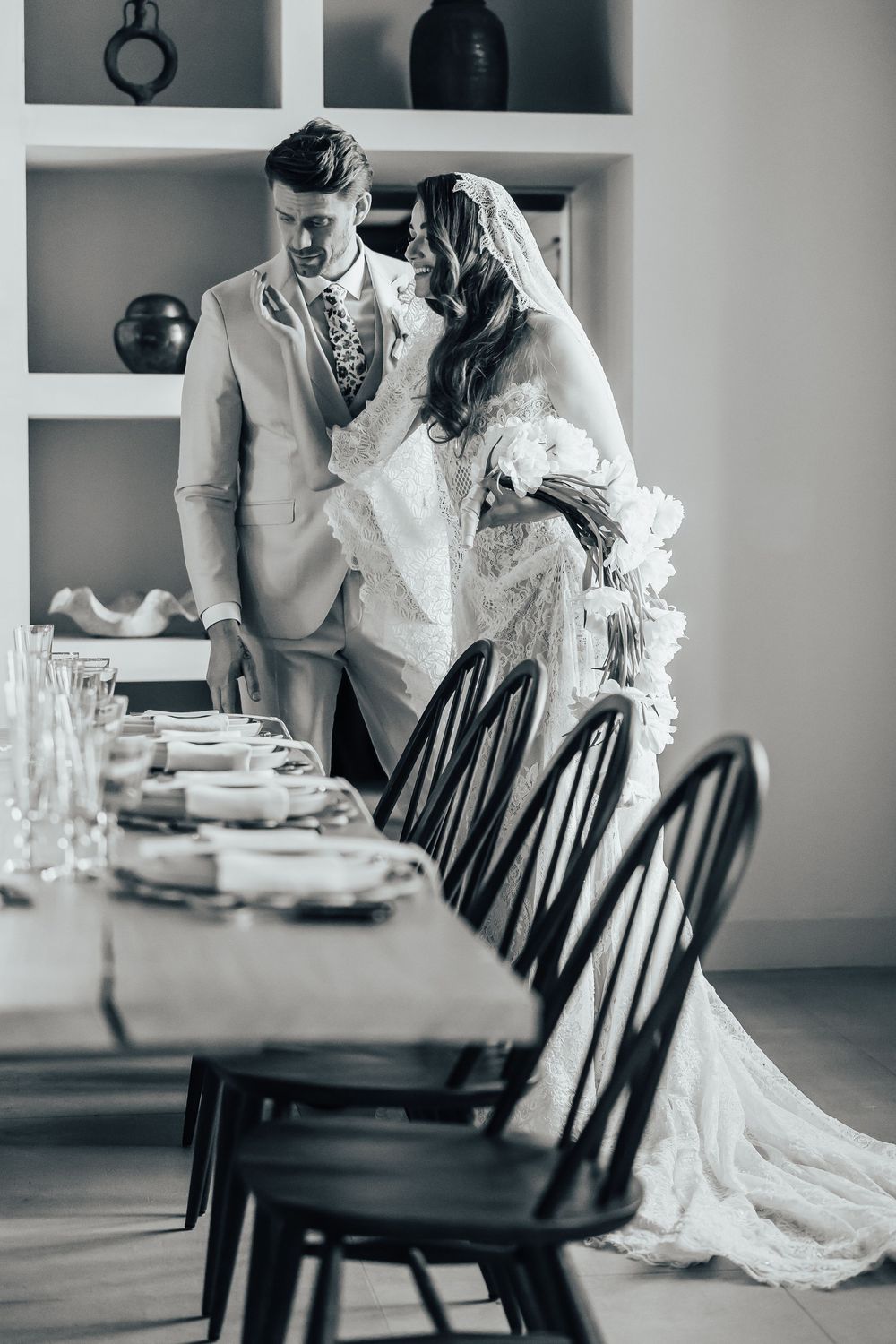 Black and white photo of a bride and groom standing together at an elegantly set dining table on their wedding day.