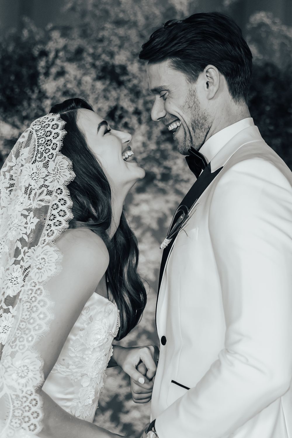 Black and white photo of a laughing bride and groom in wedding attire sharing a joyful moment together.
